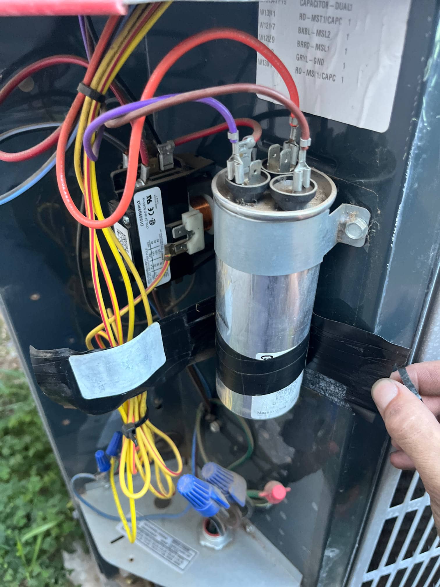 Dual-run capacitor with connected terminals beside the contactor, with yellow control wiring and wire-nut connections visible inside the condenser.