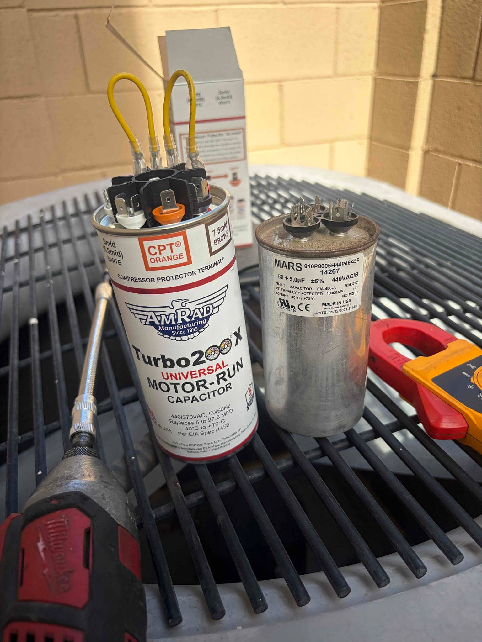 Dual-run capacitor labeled 80 + 5 μF 440VAC sits beside a universal motor-run capacitor and tools on the condenser.
