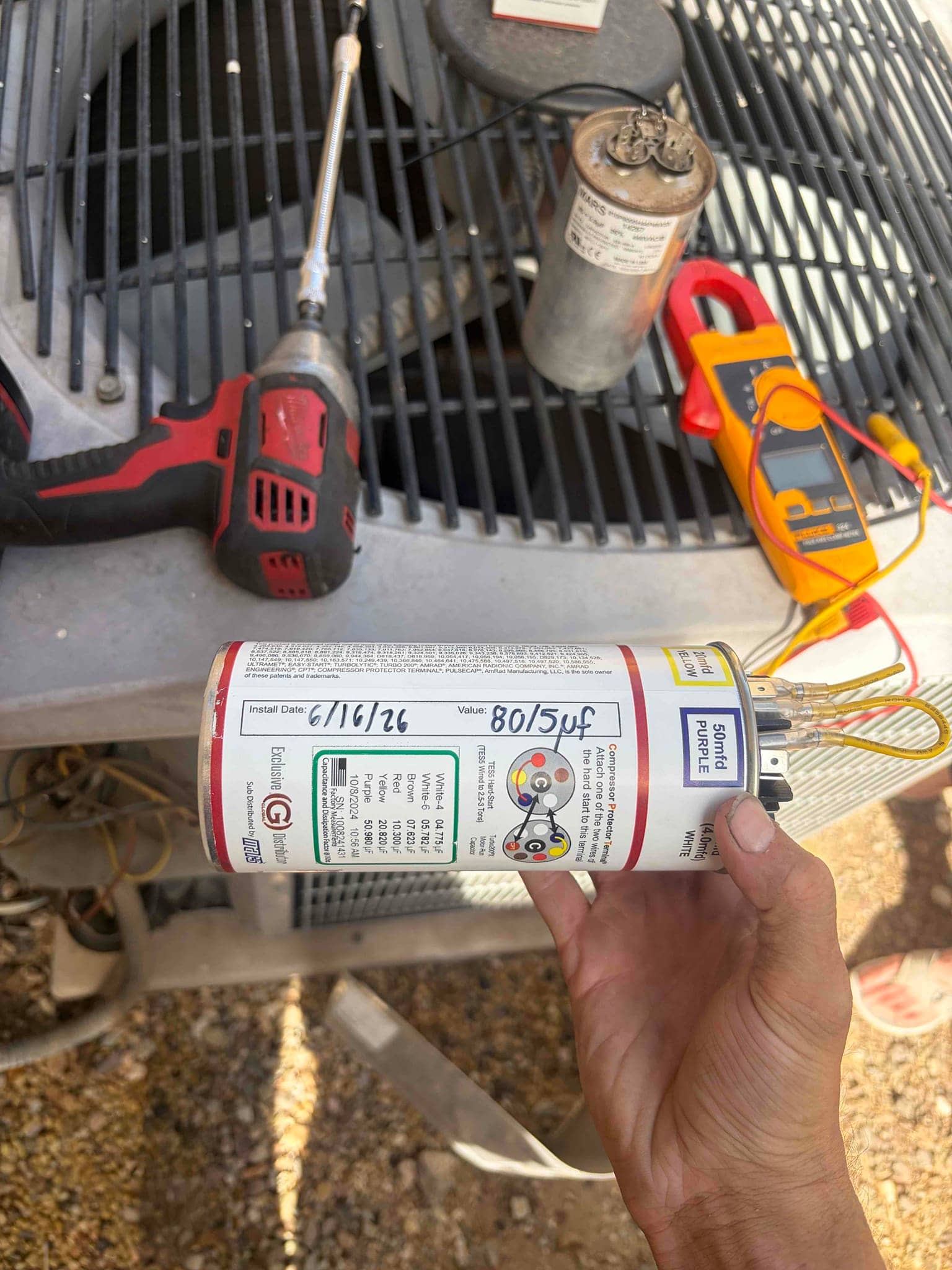 Dual-run capacitor labeled 80/5 μF with wiring terminals, shown alongside clamp meter and cordless driver.