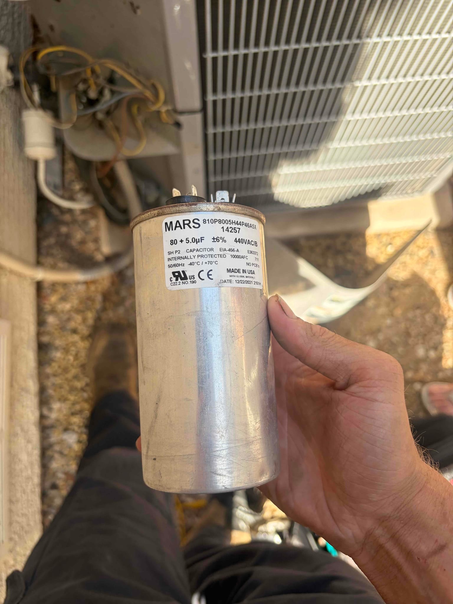 Dual-run capacitor labeled 80 + 5 μF, 440VAC, with wiring terminals visible, held near outdoor condenser unit.