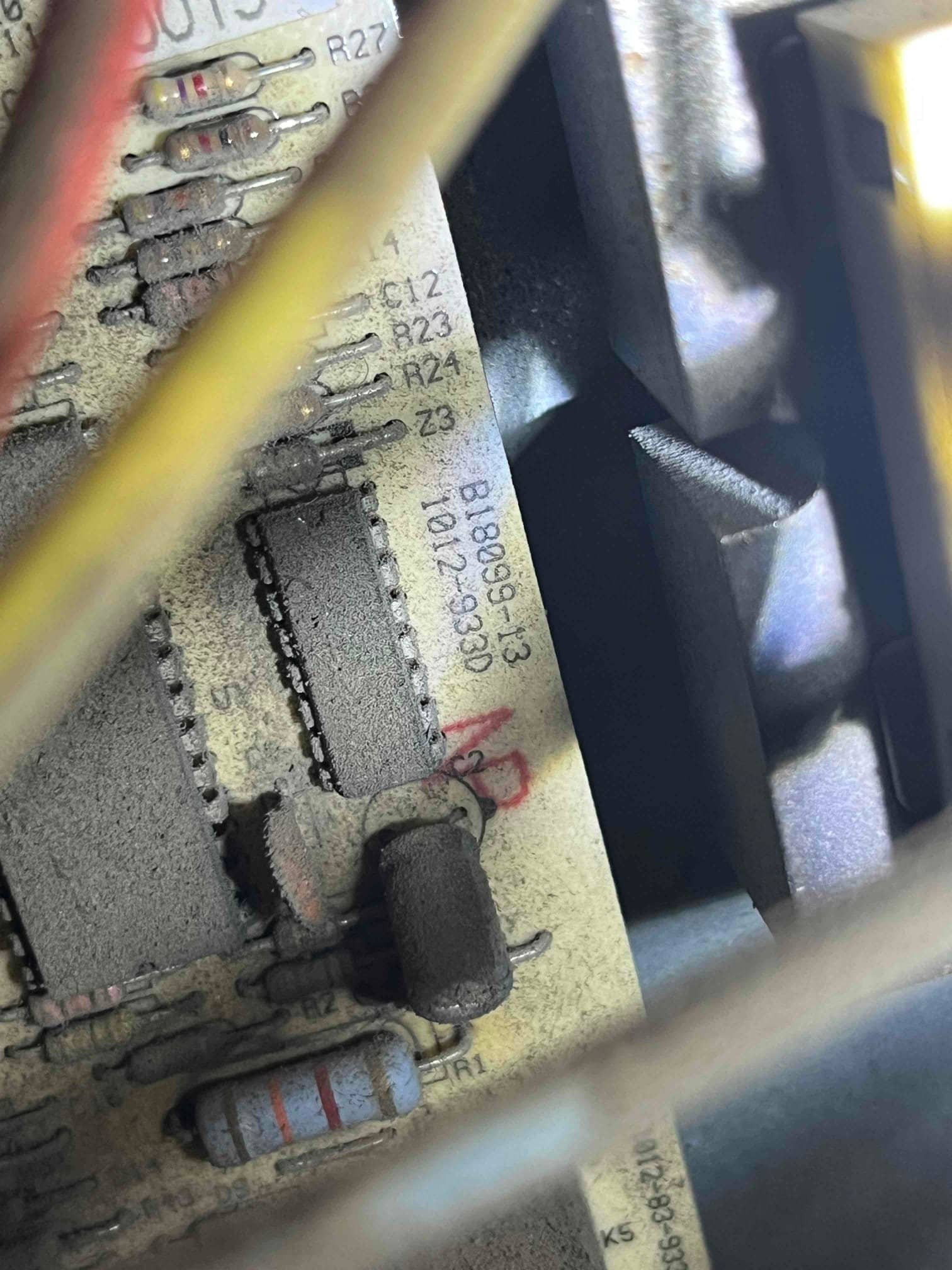 Dust-covered control board inside HVAC unit showing resistors, integrated circuits, and printed designators R27, C12, R24 near wiring.