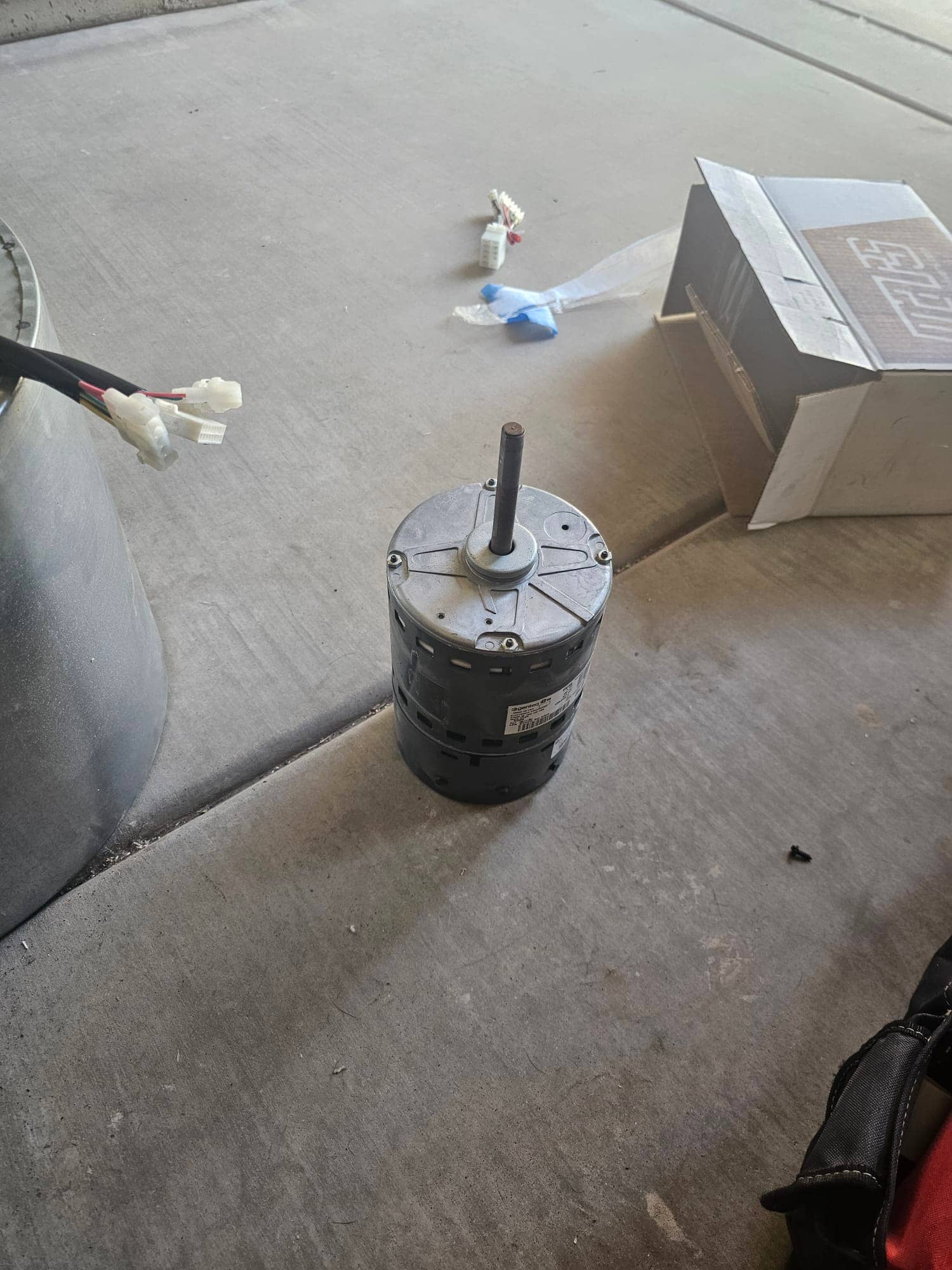 Electric motor with vertical shaft placed on the ground, with wiring connectors and an open parts box nearby.