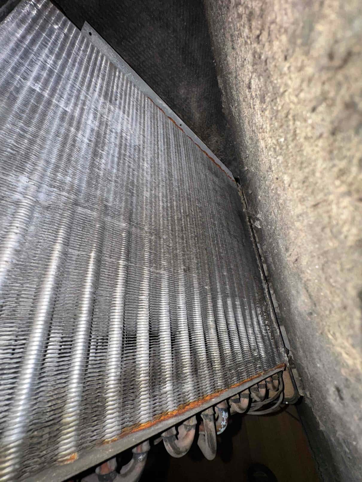 Evaporator coil with aluminum fins and copper tubes, visible rust along the lower edge.