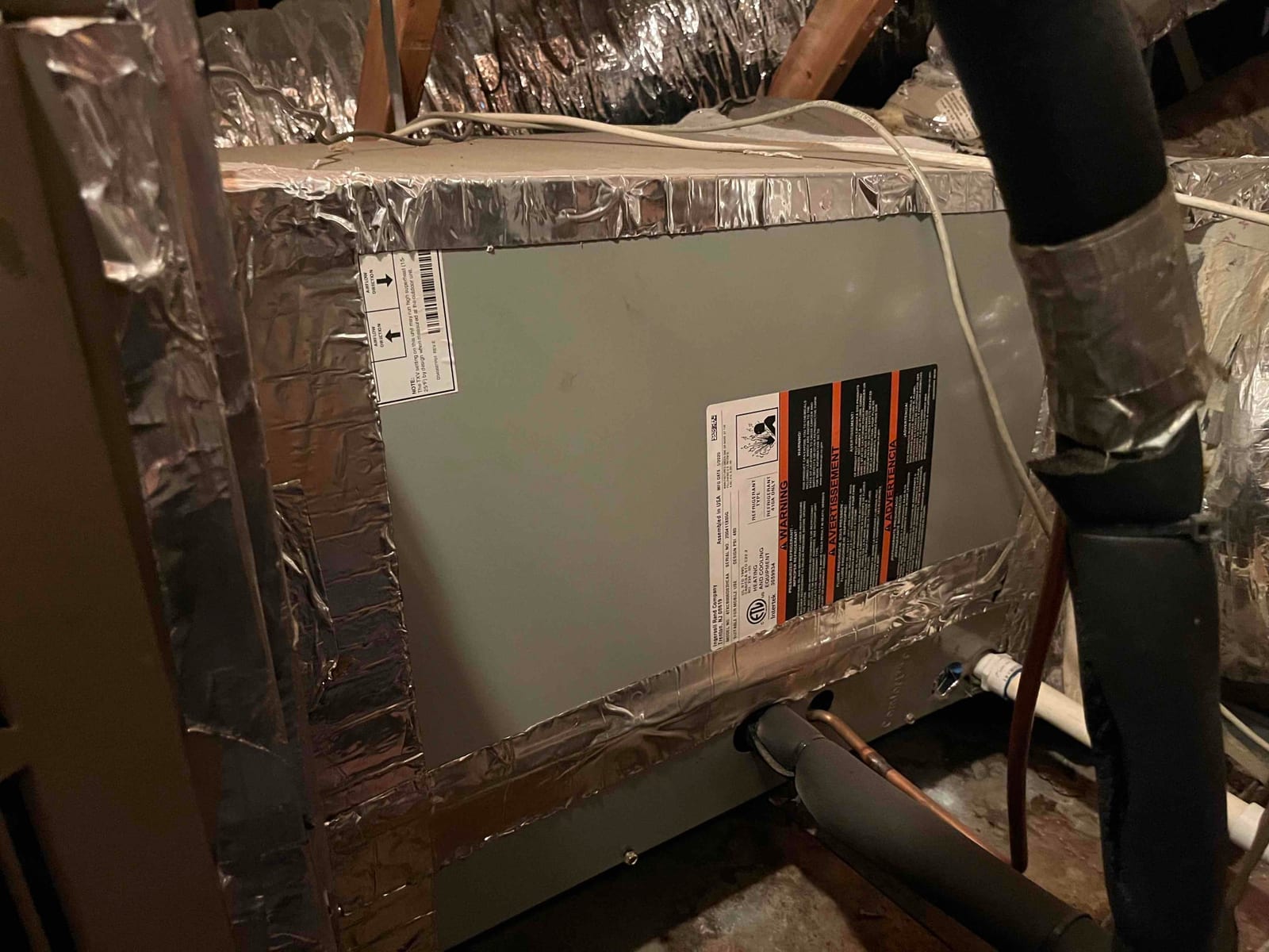Evaporator coil cabinet in attic with foil-taped seams, insulated refrigerant lines, and PVC condensate drain connections visible.