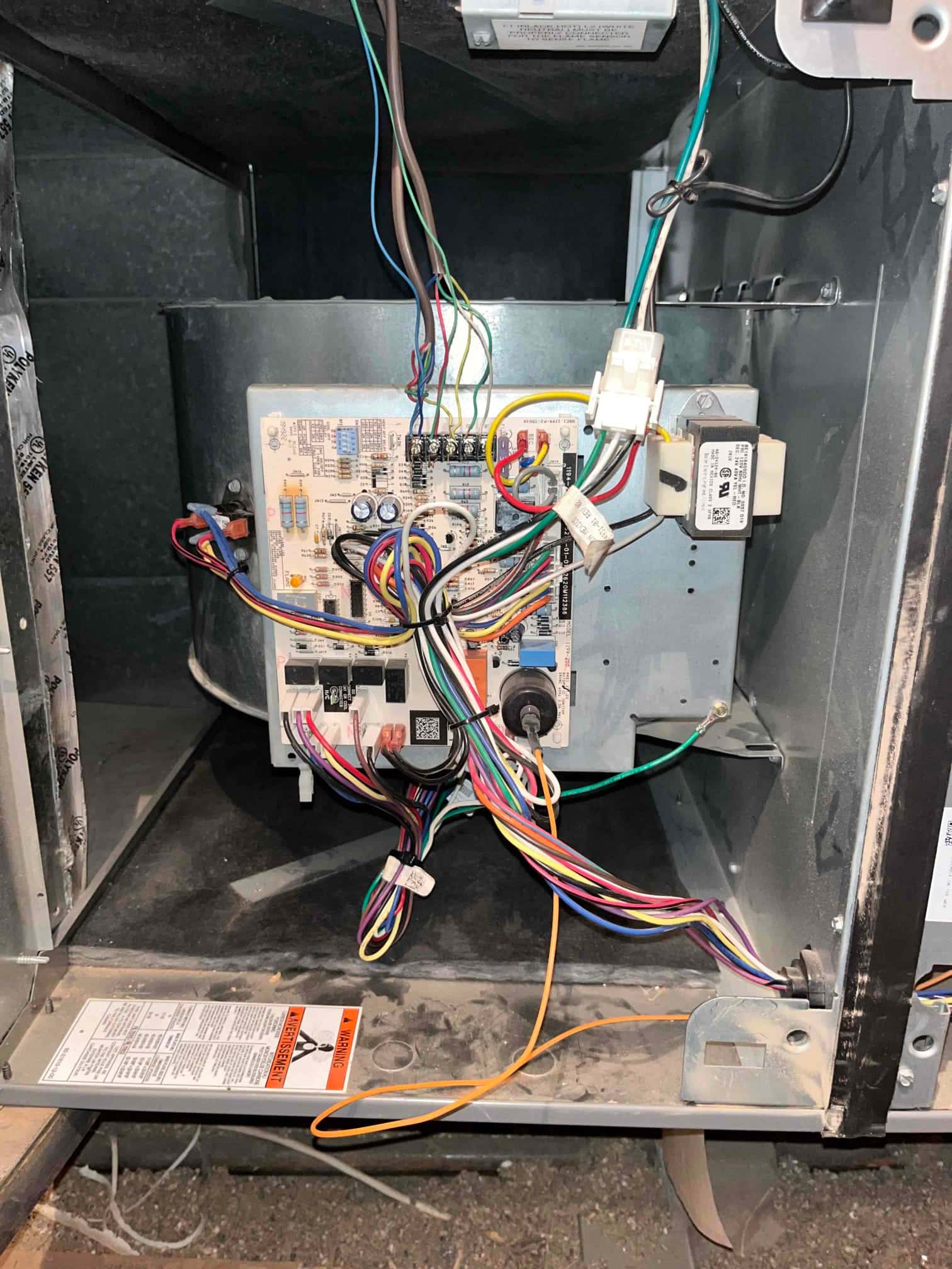 Furnace control board with connected wiring harness and transformer exposed in blower compartment during service, panel removed.