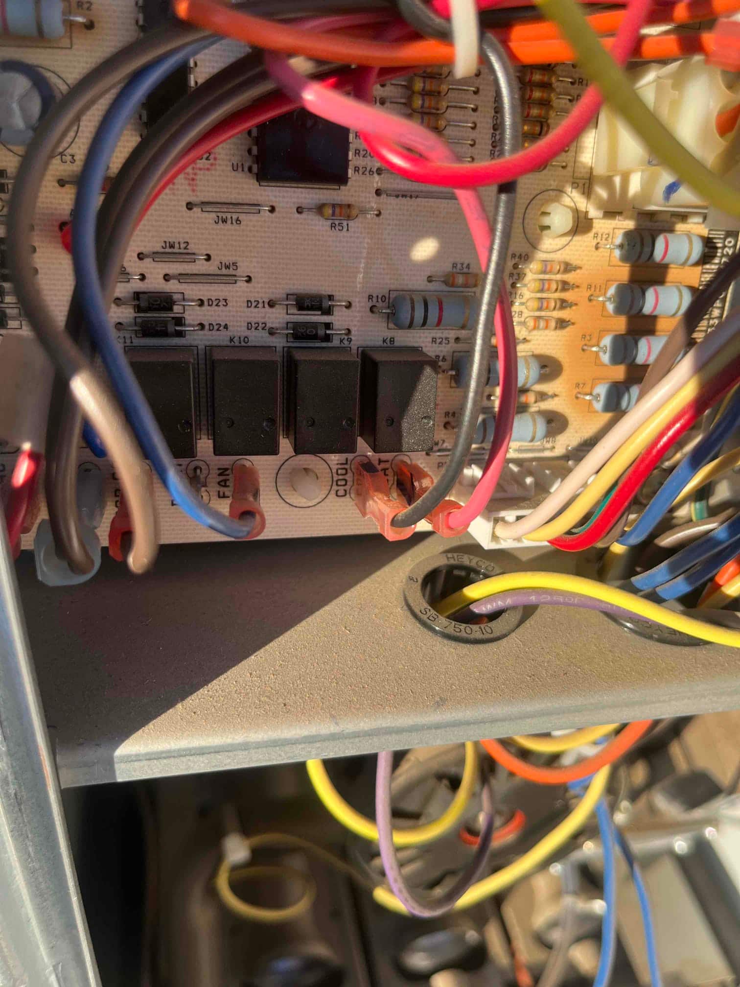 HVAC control board inside cabinet, showing relays, resistors, and multiple colored wires connected at labeled terminals.