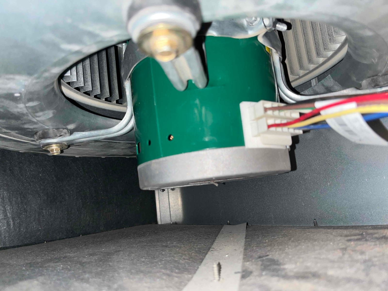 Indoor blower motor inside air handler showing electrical plug connector, wiring harness, and blower wheel blades within the housing.
