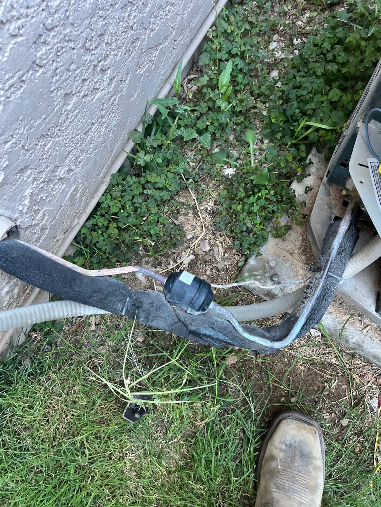 Insulated refrigerant lines at the outdoor condenser with cracked foam insulation and an inline component exposed near ground.