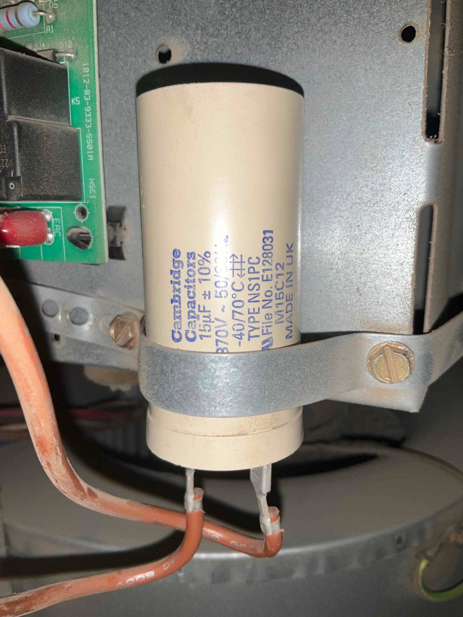 Motor run capacitor labeled 15 μF ±10% 370V 50/60Hz, mounted with a metal strap, with two orange leads connected.