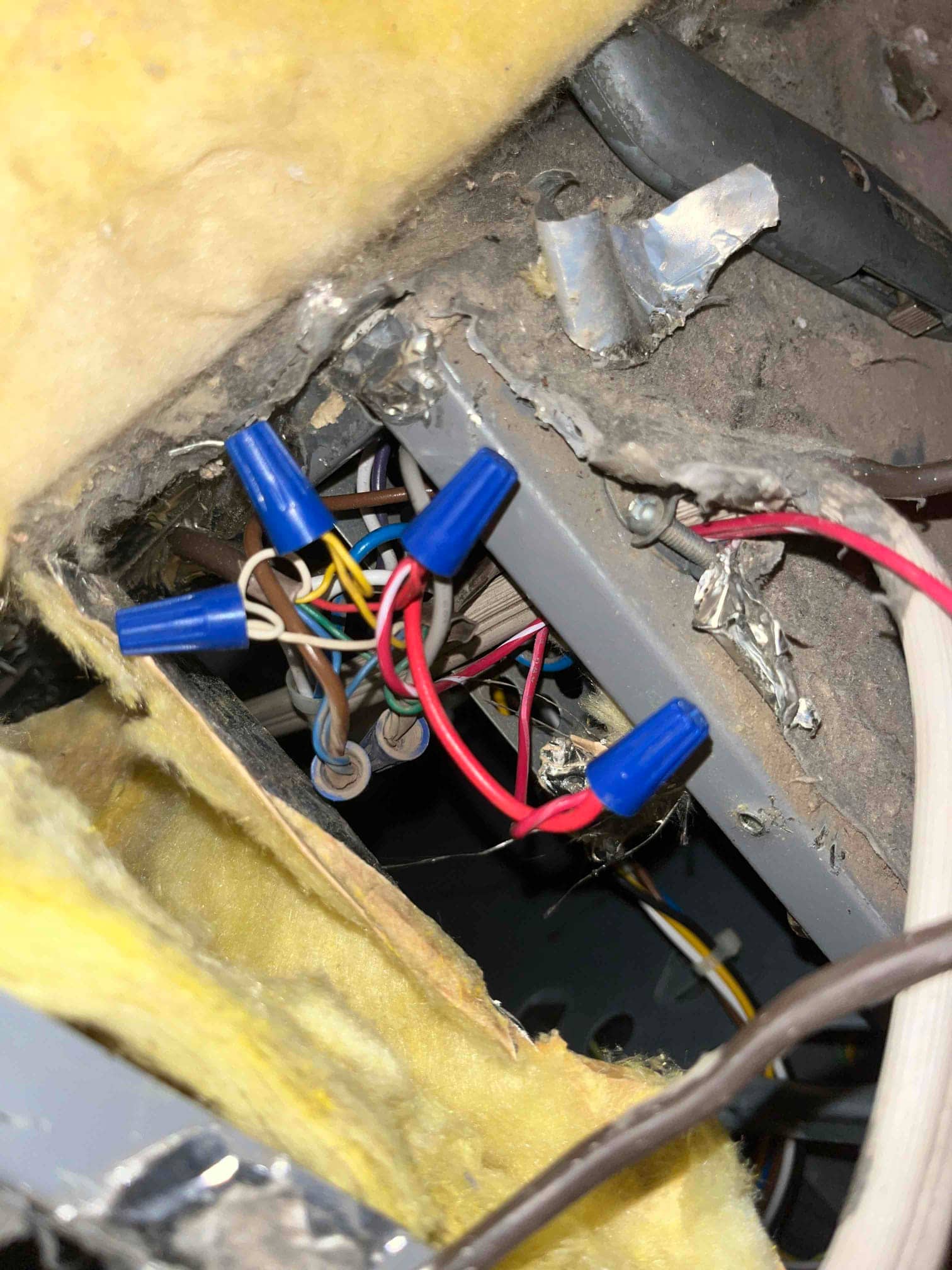 Multiple low-voltage and power wires joined with blue wire nuts inside an air handler cavity beside yellow insulation.