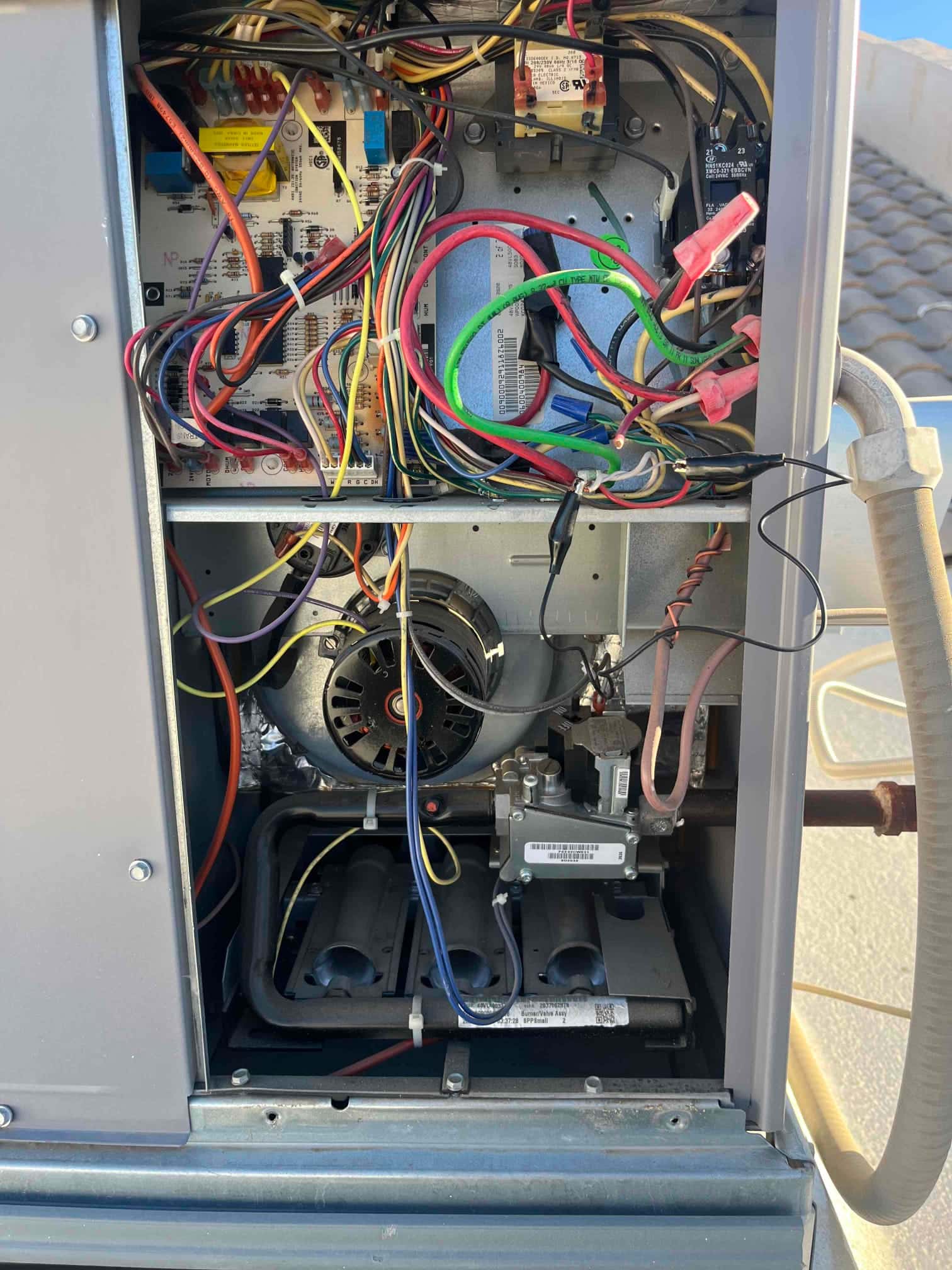 Open furnace cabinet showing control board wiring, multiple connectors, motor housing, gas valve assembly, and three burner tubes.