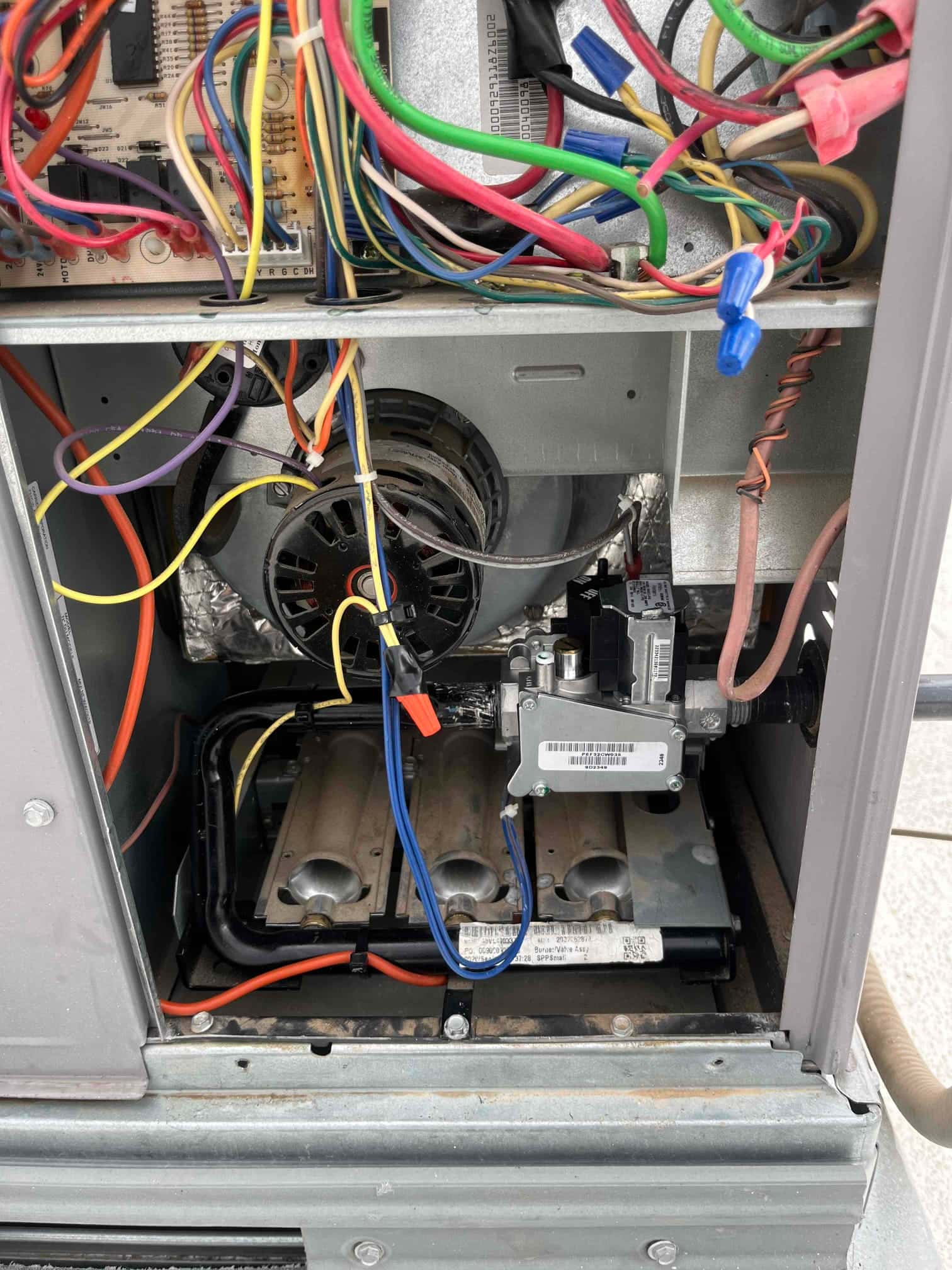 Open gas furnace cabinet showing control board wiring, inducer motor, gas valve with tubing, and three-burner assembly inside the lower compartment.
