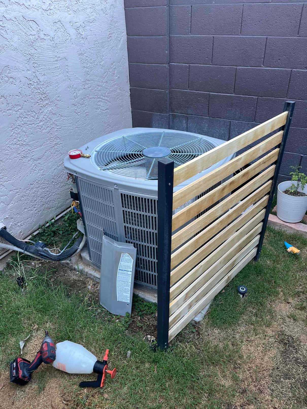 Outdoor condenser unit with service panel removed; wiring exposed on the side. Tools and privacy screen nearby.