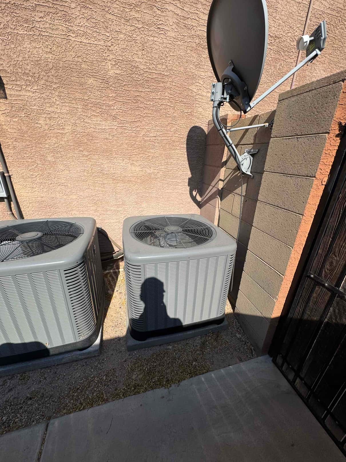 Two outdoor condenser units installed on pads beside a stucco wall, fan grills visible.