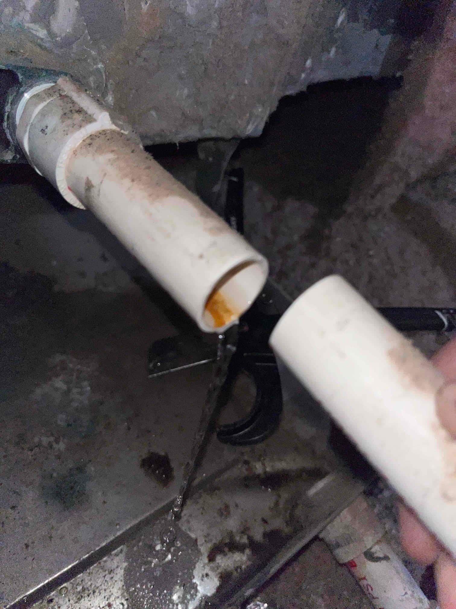 PVC condensate drain line disconnected at a coupling, with water flowing onto the drain pan below.