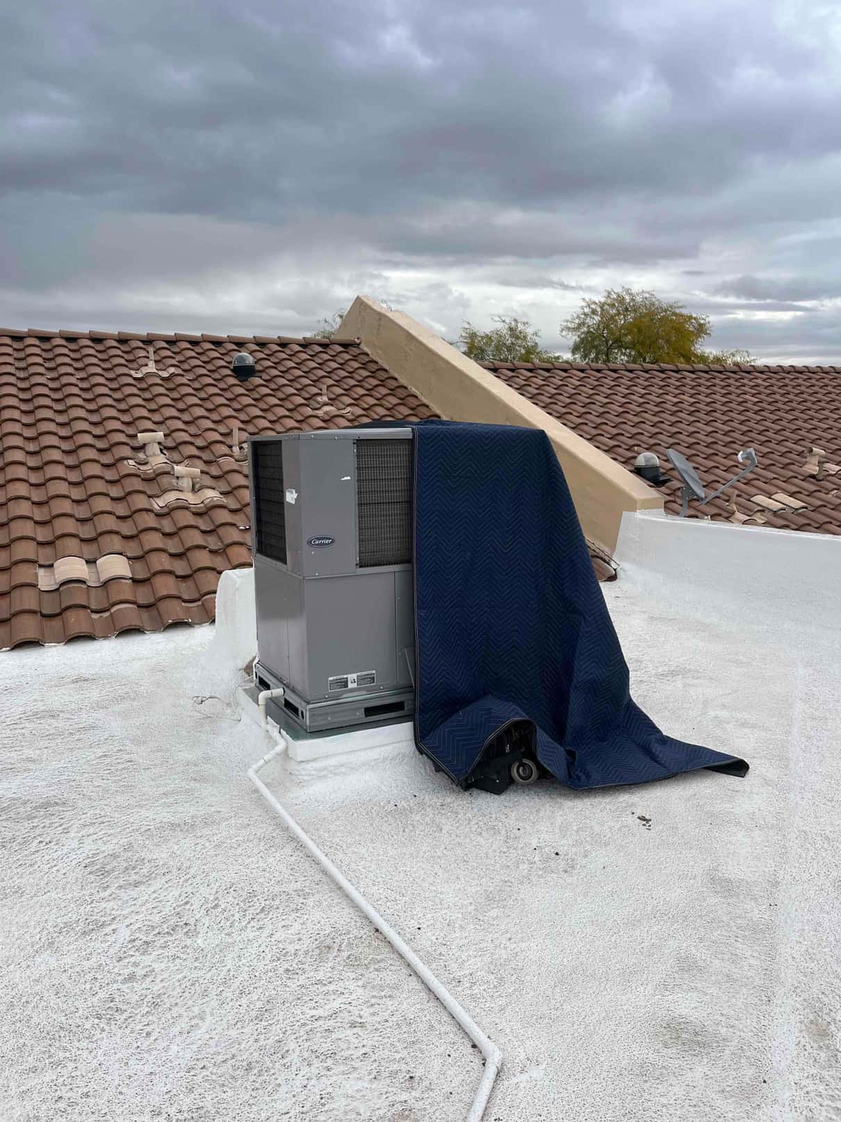 Rooftop packaged HVAC unit on curb mount with a moving blanket draped over one side.
