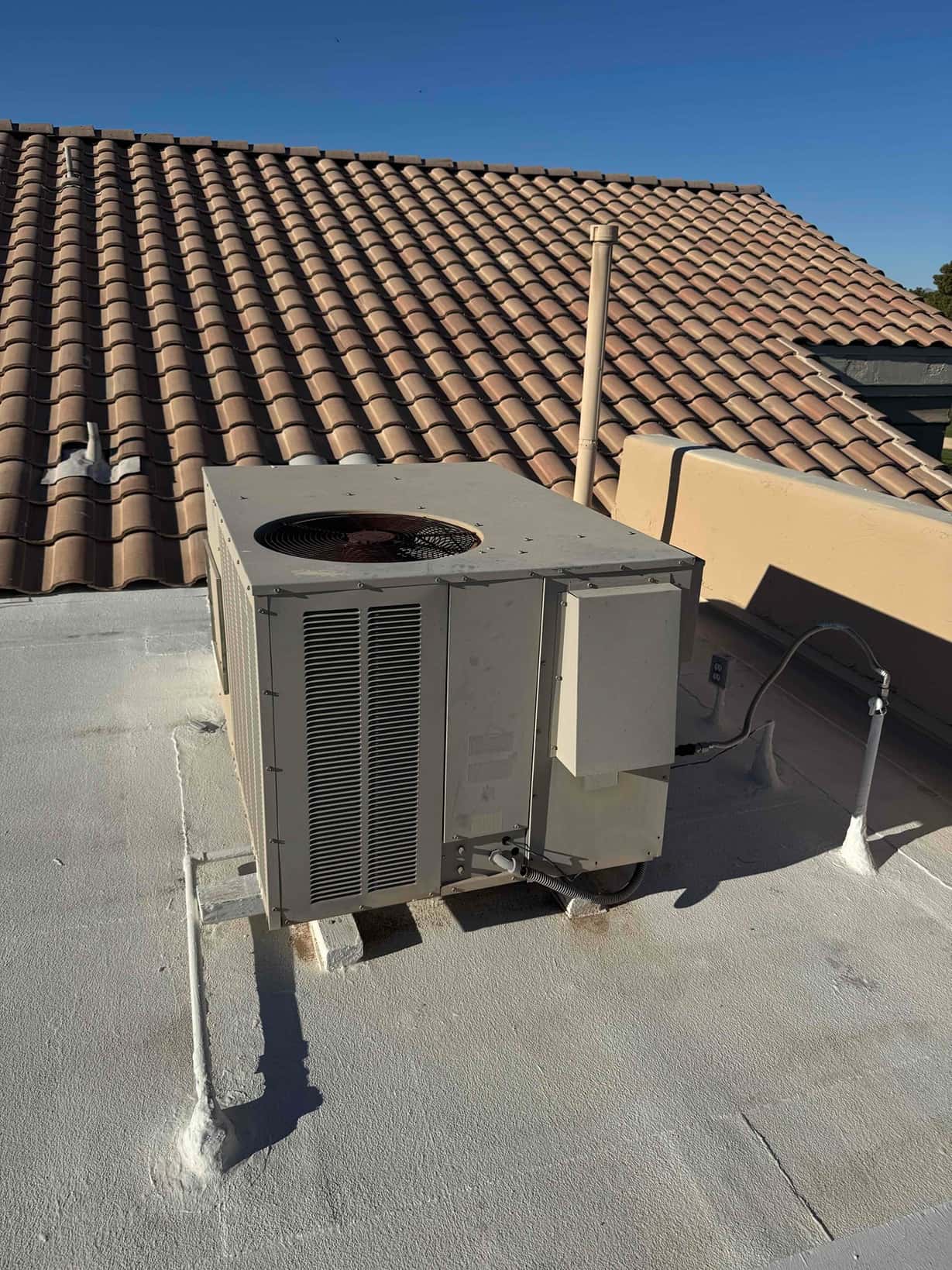 Rooftop packaged HVAC unit on curb supports with electrical conduit and service disconnect visible.