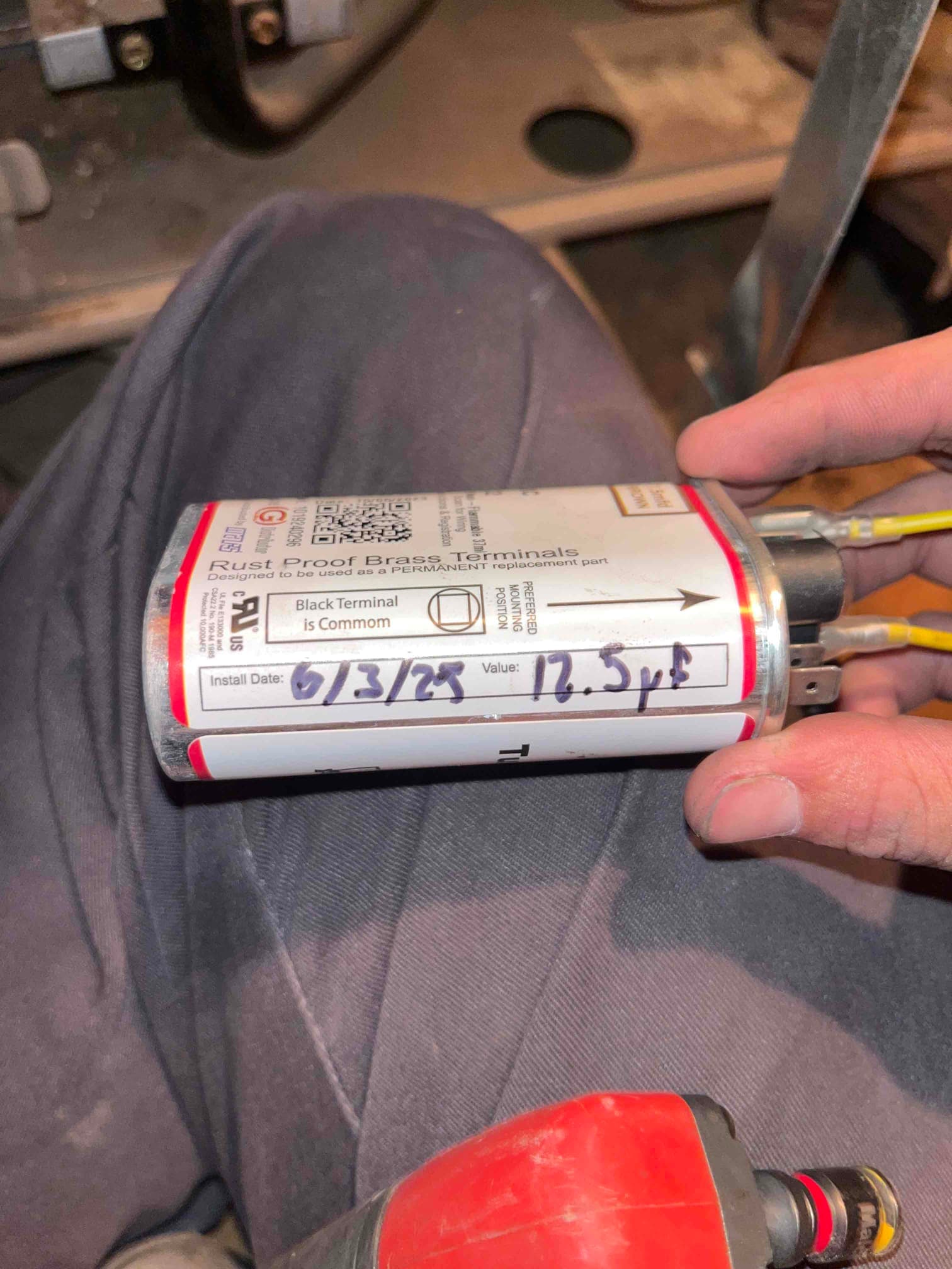 Run capacitor held in hand, with handwritten install date and noted value 12.5 μF on the label.