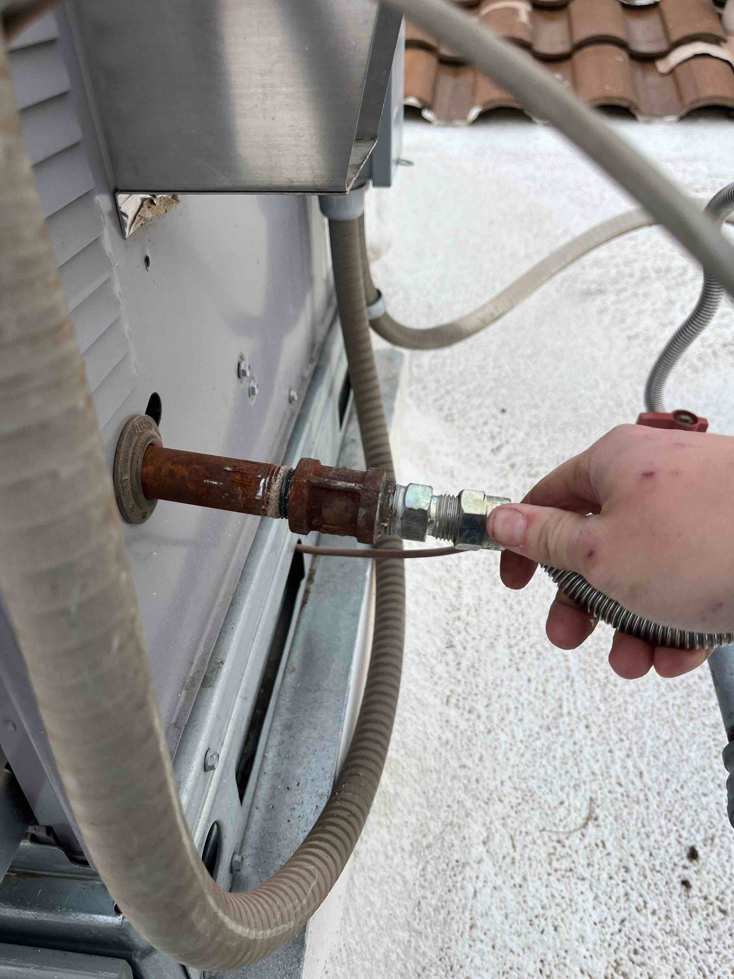 Rusty gas line connection at a rooftop unit, with a technician’s hand holding a flexible connector.