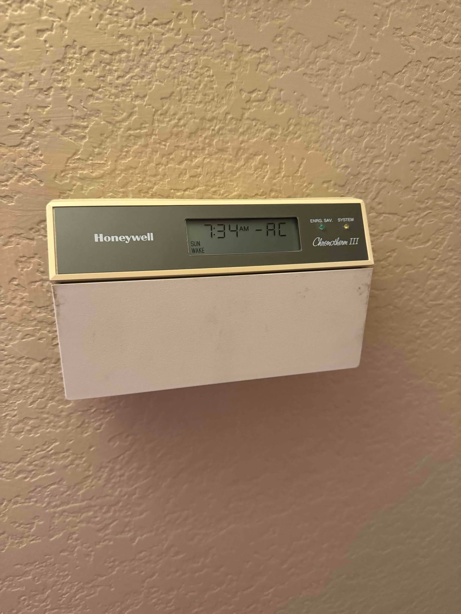 Wall-mounted digital thermostat with LCD display showing 7:34 AM and AC mode status.