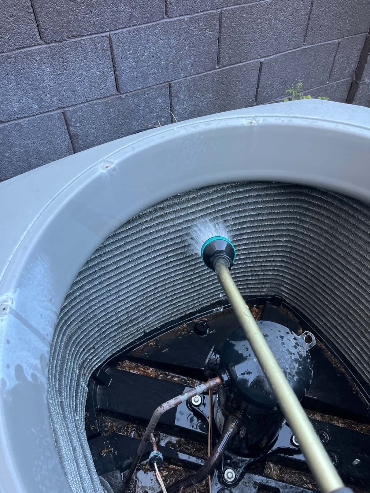 Water spray rinses the condenser coil interior while compressor and base pan are visible.