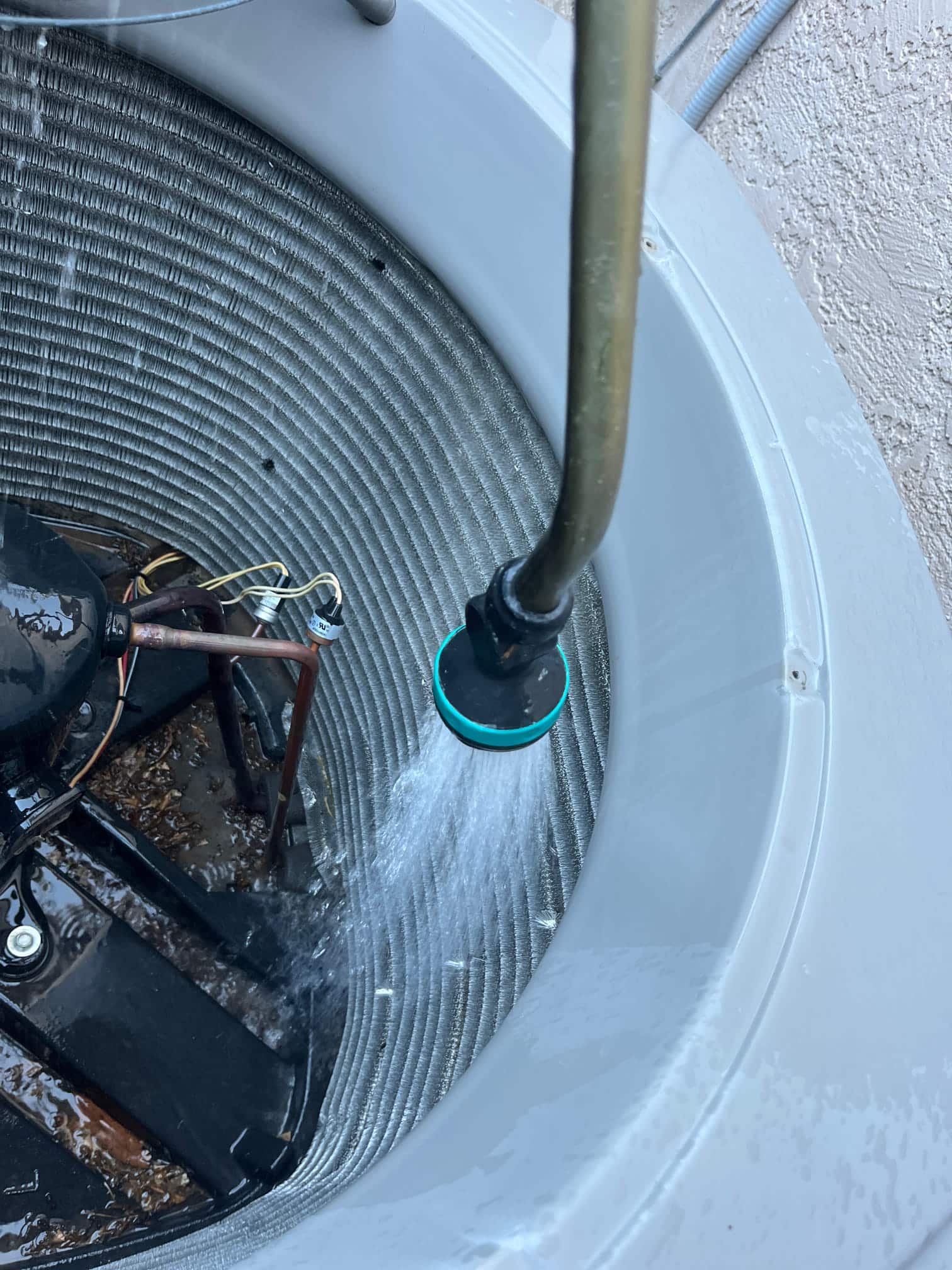 Water sprayer rinses debris from the condenser coil inside an outdoor unit housing.