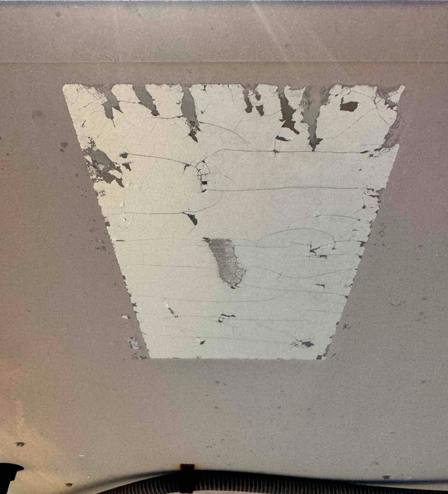 Worn and peeling equipment label adhesive on a metal HVAC cabinet panel near flexible conduit.