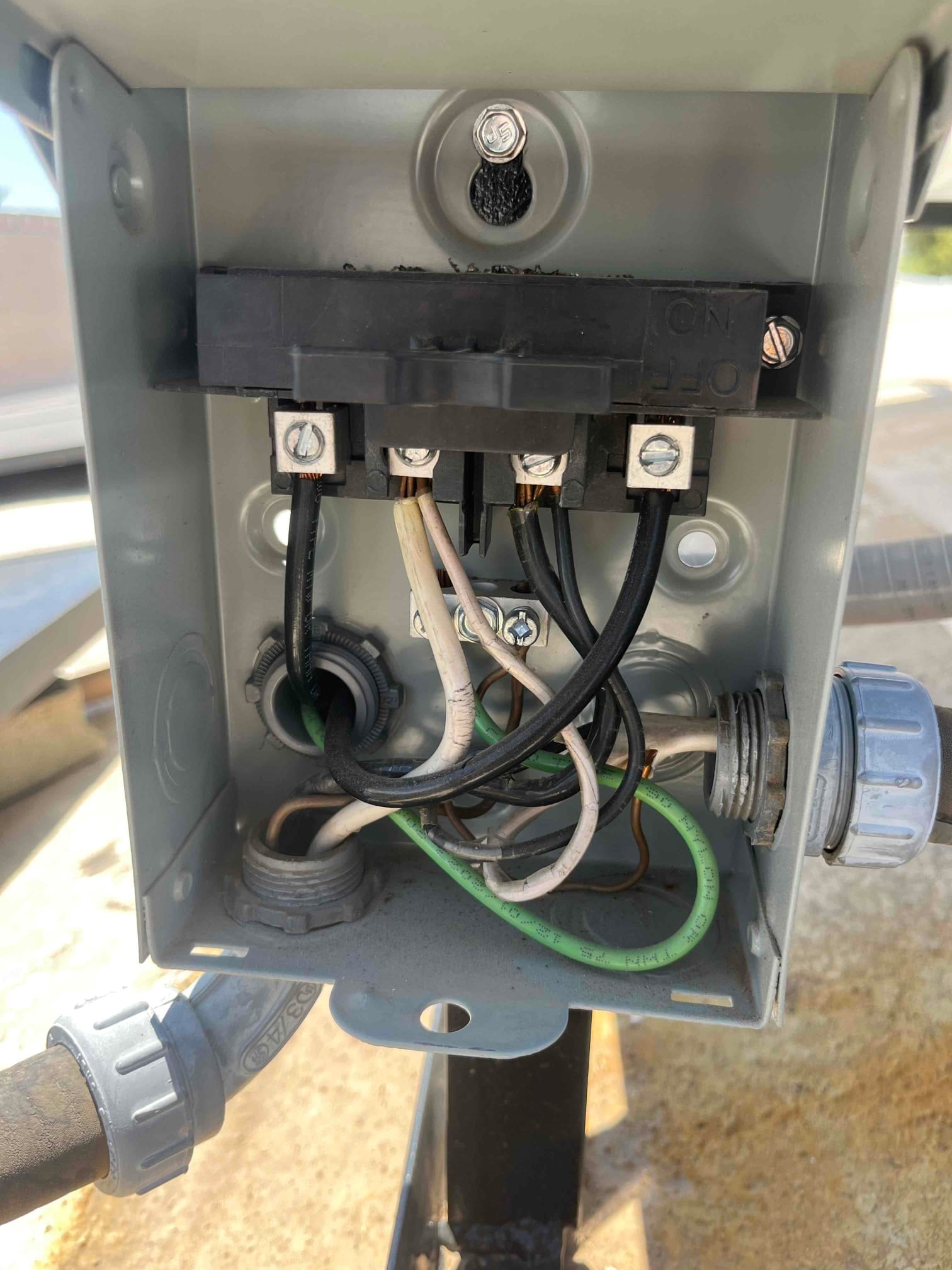 Air conditioner outdoor disconnect box open, showing pull-out switch and connected black, white, and green conductors with strain relief fittings.