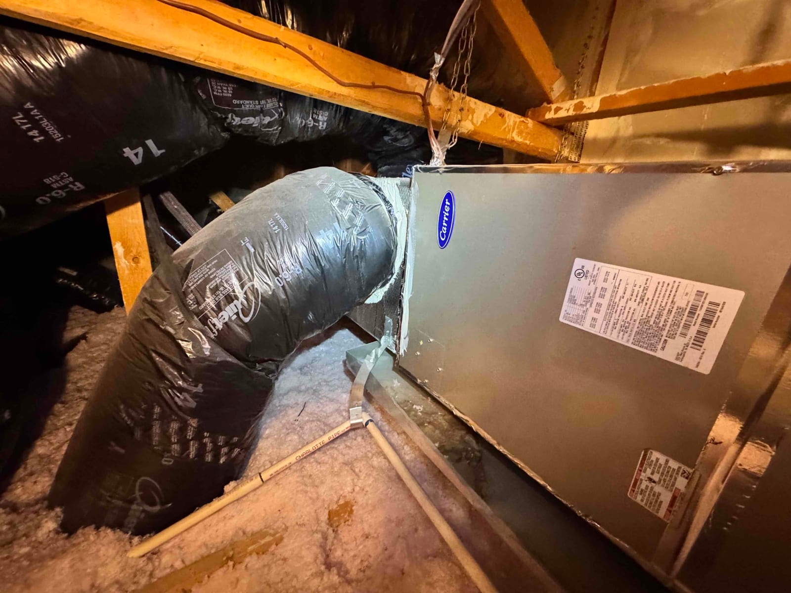 Air handler in attic with insulated flex duct connections and condensate drain line over attic insulation.