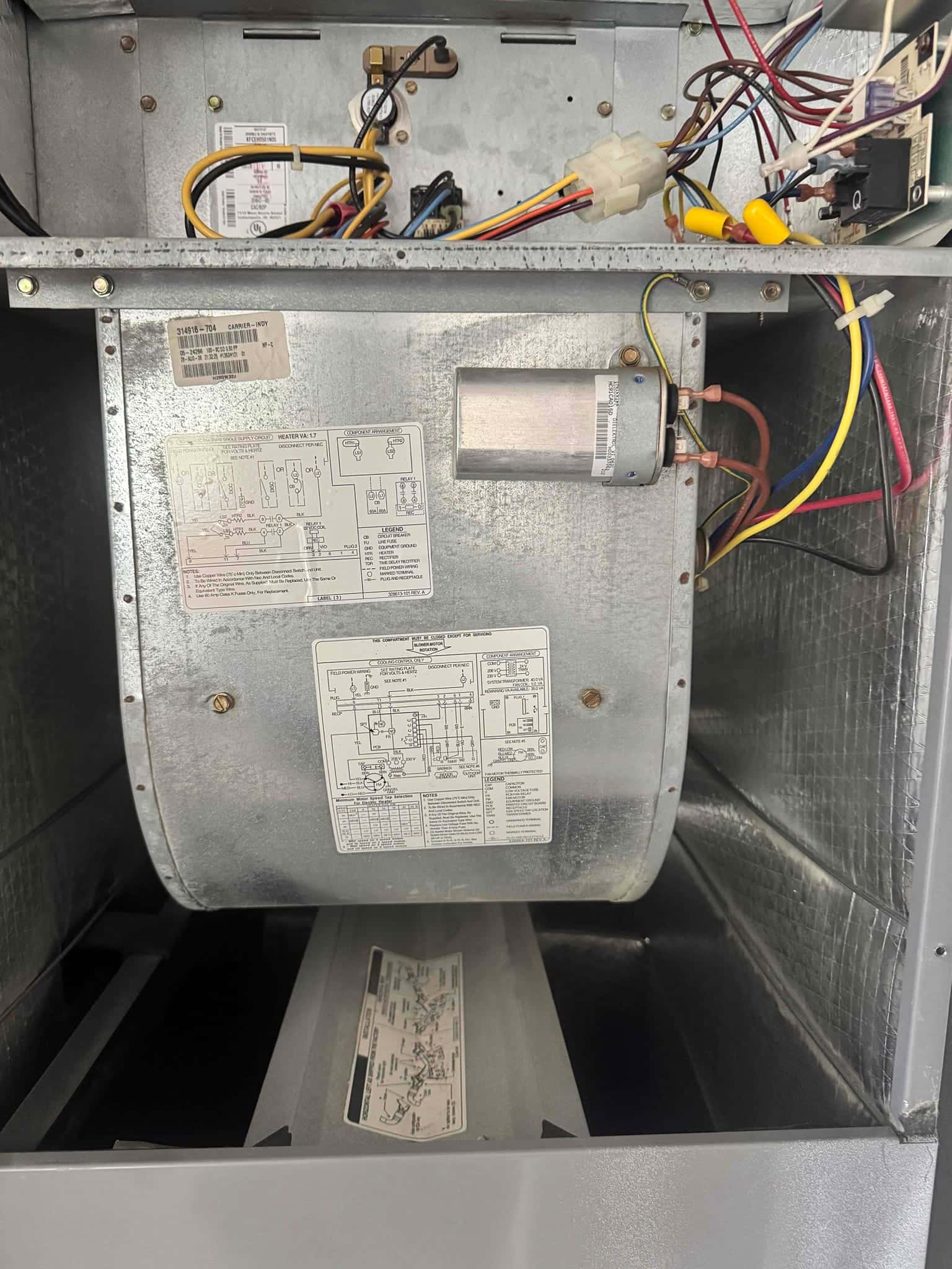Air handler blower compartment open, showing blower housing, dual-run capacitor with connected wiring, and control components.