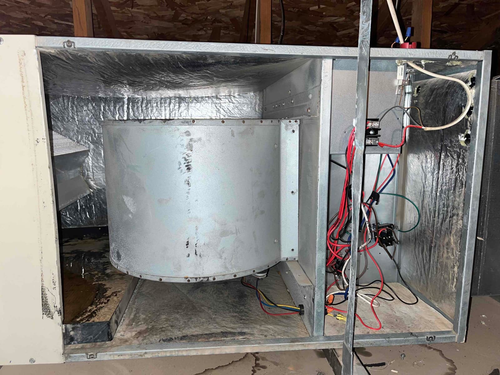 Air handler blower housing and open control compartment with wiring exposed; standing water visible in the drain pan.