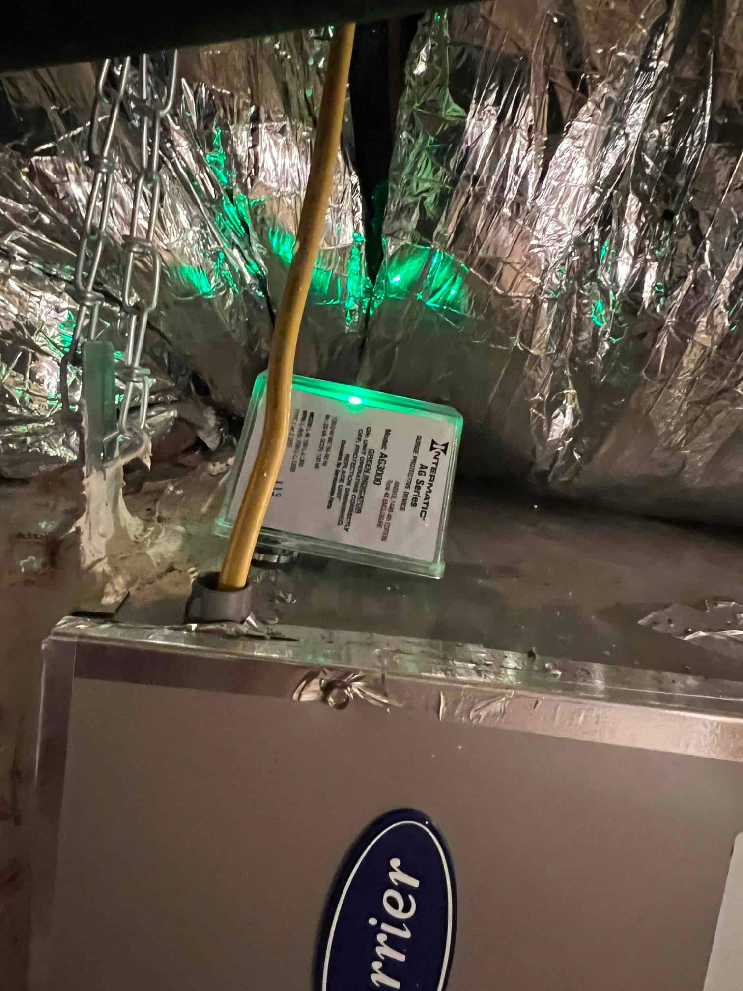 Air handler cabinet with insulated ductwork and a small electronic module mounted nearby showing a green indicator light.