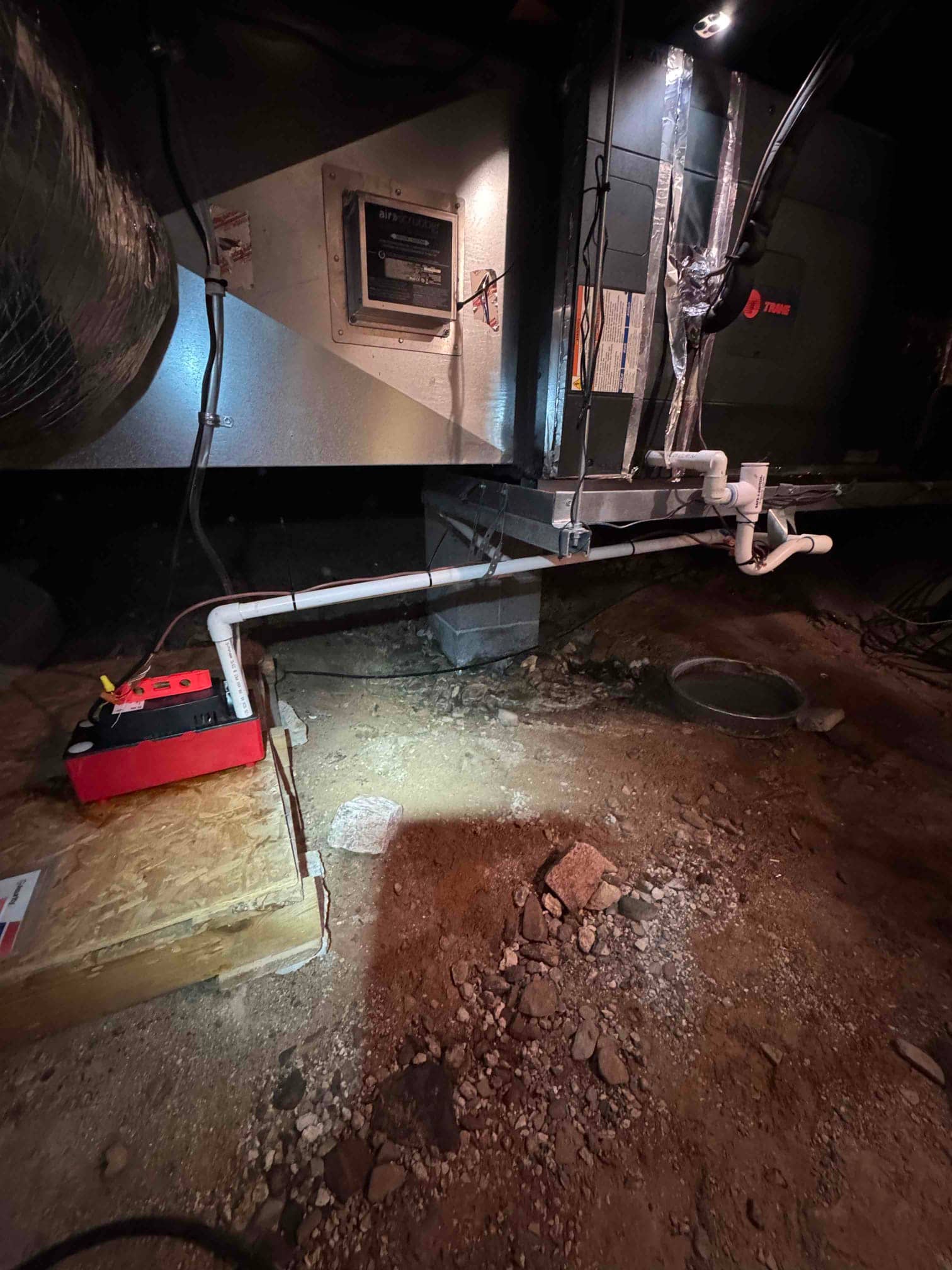 Air handler in crawlspace with insulated duct connection and PVC condensate drain with trap and cleanout fittings.