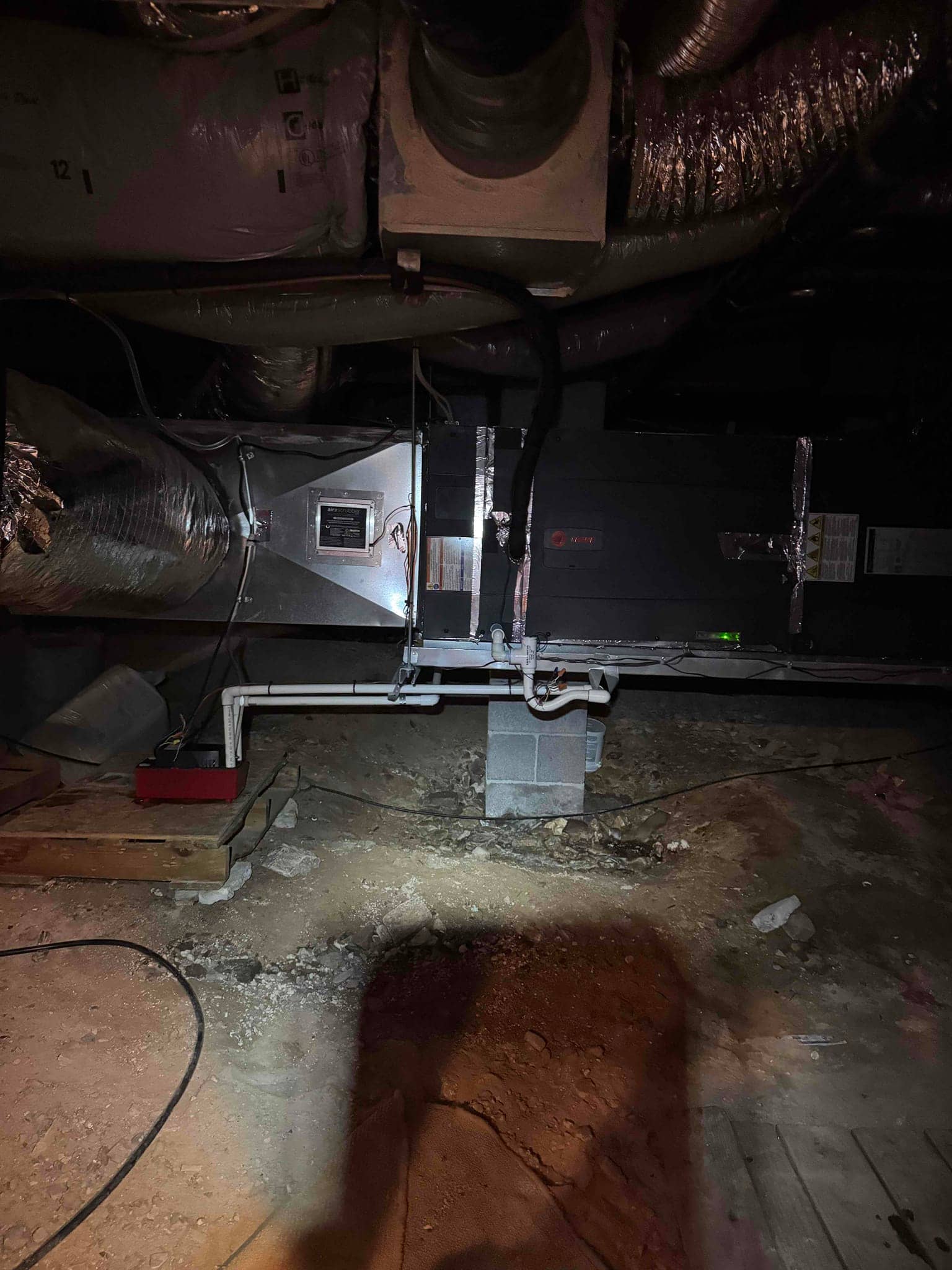Air handler in crawlspace with insulated ducts and PVC condensate drain lines supported on blocks.