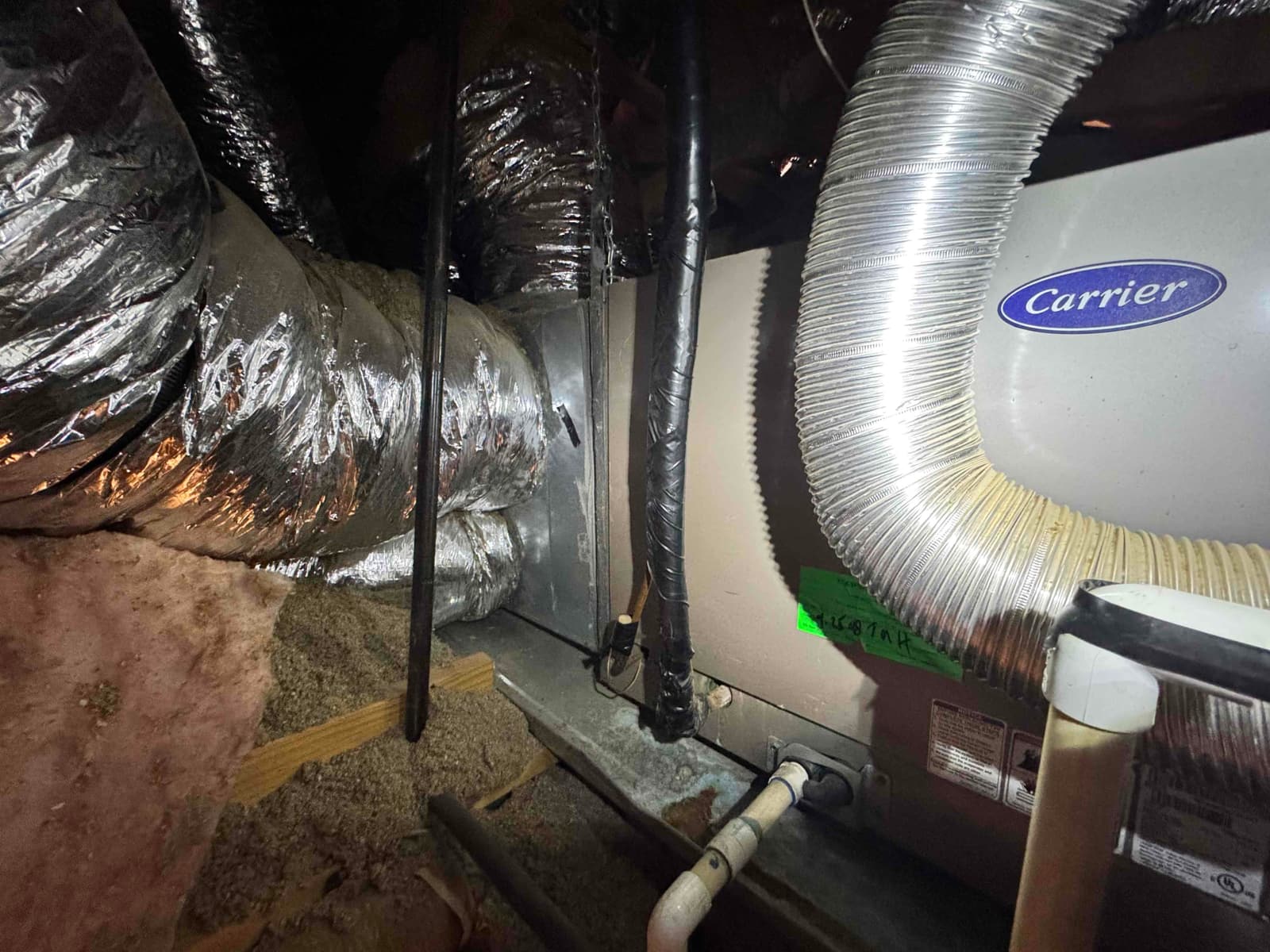 Attic air handler with flexible supply and return ducts, insulated refrigerant line, and condensate drain piping visible.