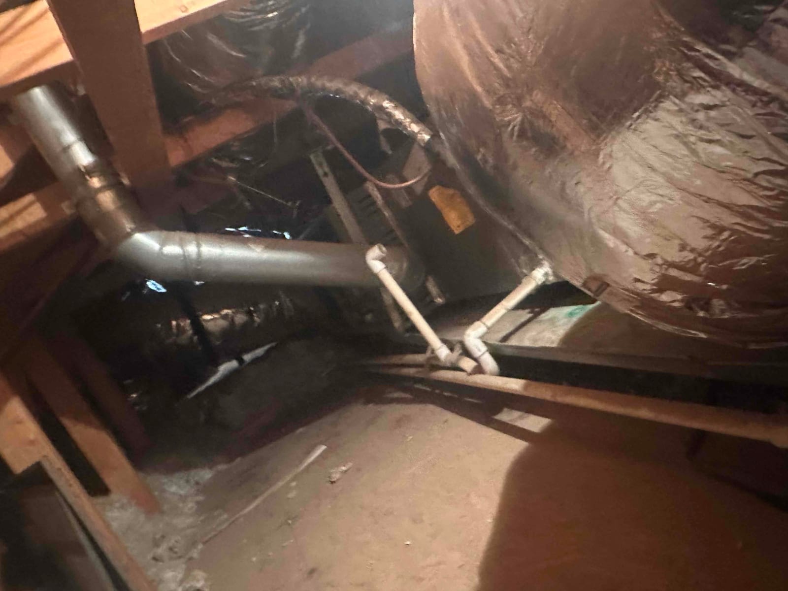 Attic air handler with insulated ductwork and PVC condensate drain lines, mounted on a support platform.