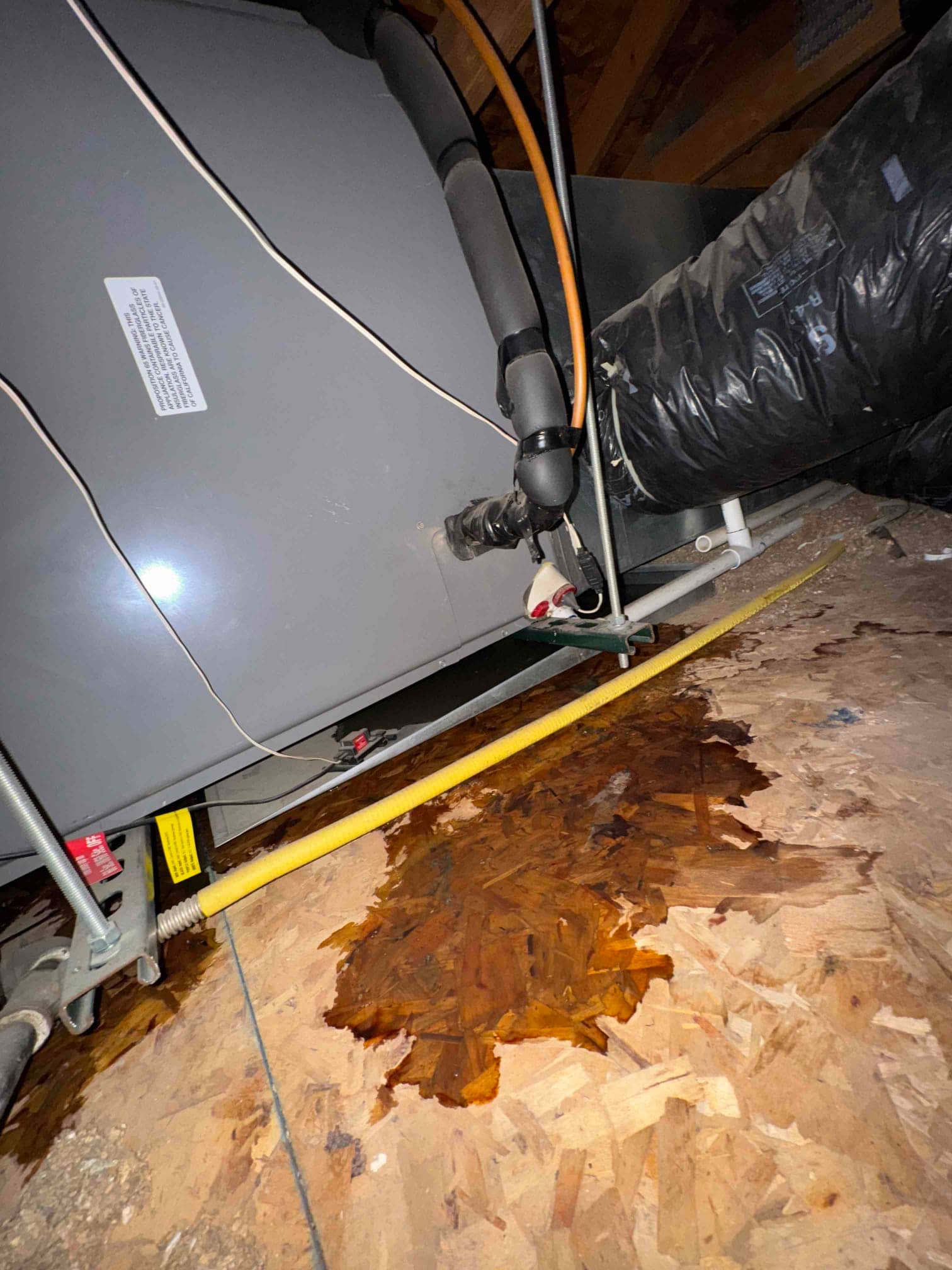 Attic air handler with insulated refrigerant lines and ductwork; dark water stain spreads across the OSB subfloor.