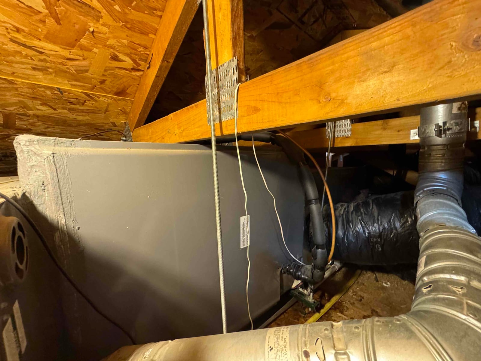 Attic air handler with insulated refrigerant lines, metal and flex ducts, and drain connections visible.