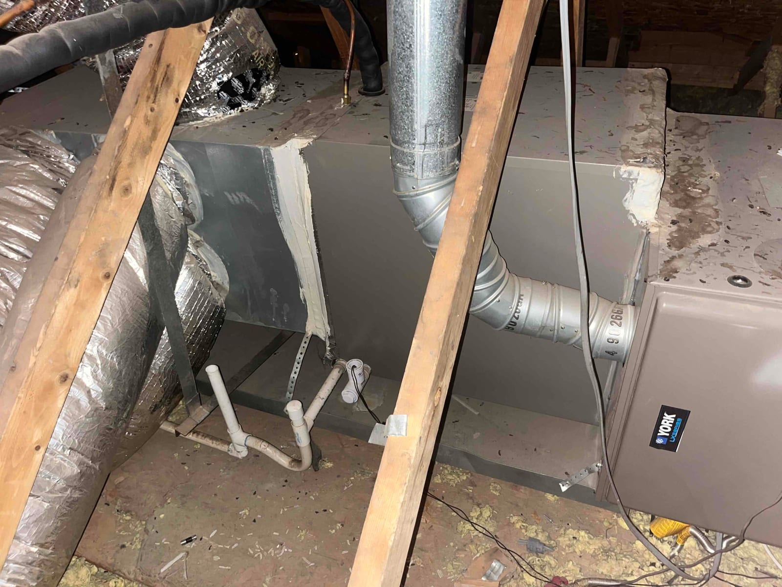 Attic furnace with sheet-metal plenum, insulated flex ducts, PVC condensate drain, and sealed joints visible around the cabinet connections.