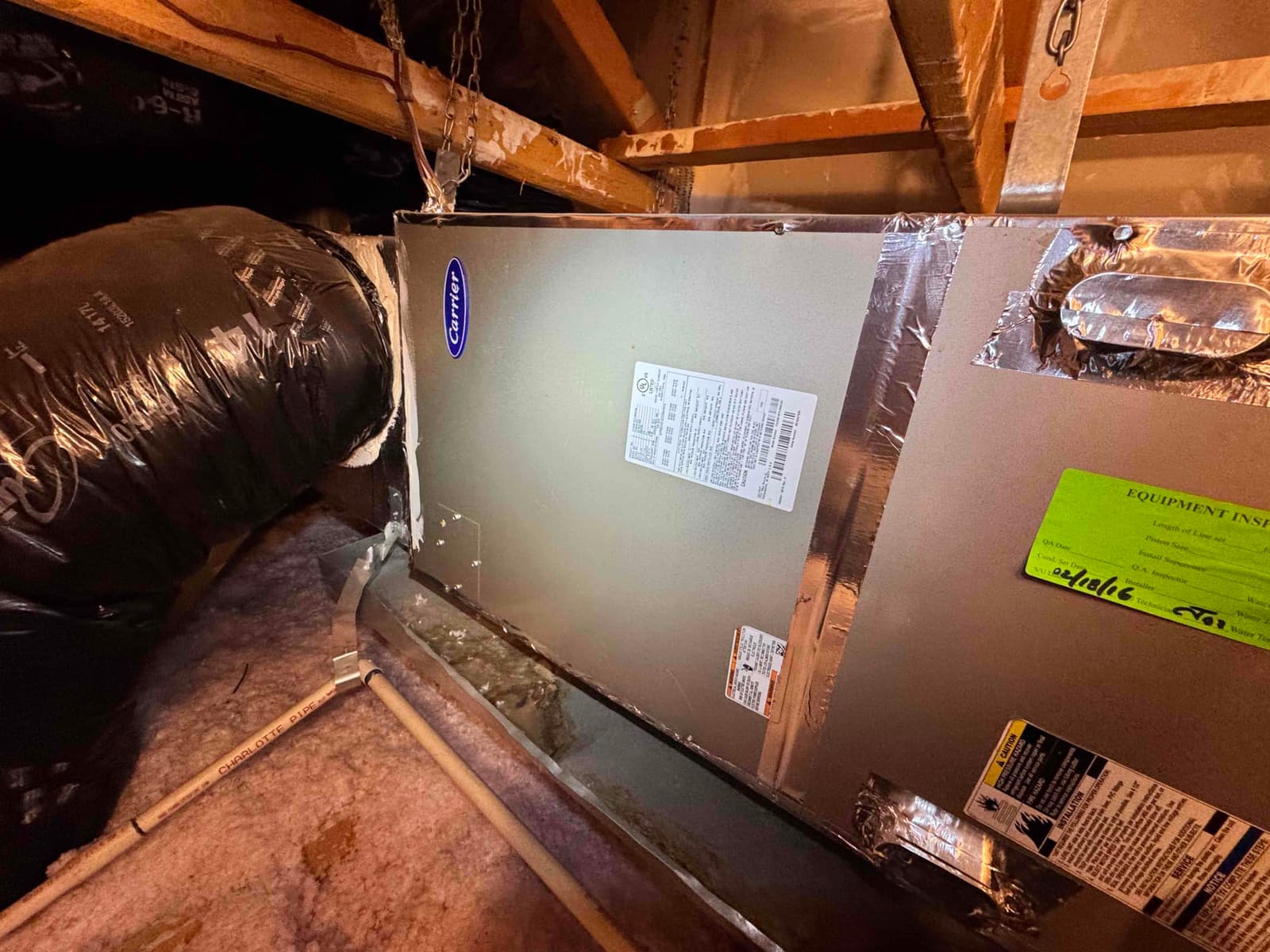 Attic-mounted air handler with insulated flex duct connection, foil-taped seams, and PVC condensate drain line along the pan.