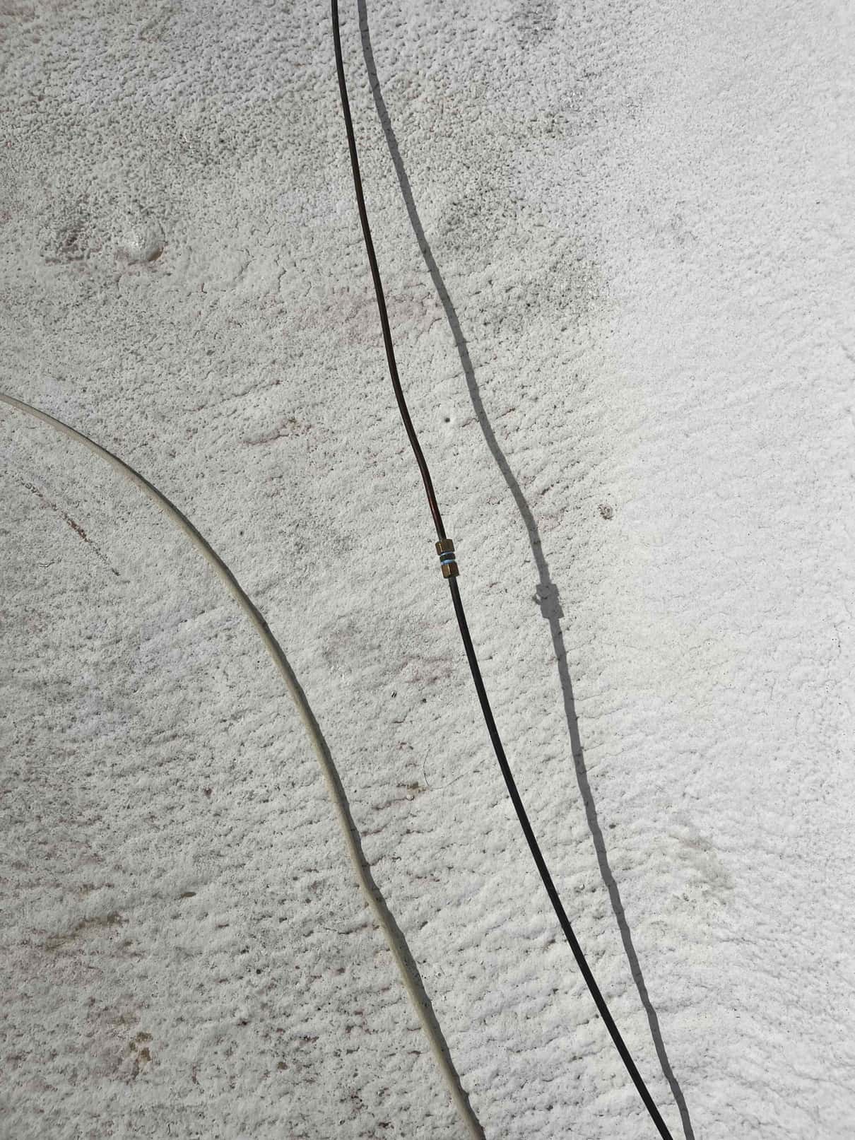 Black flexible hose lying on textured surface with a brass coupling in the middle, casting a shadow.