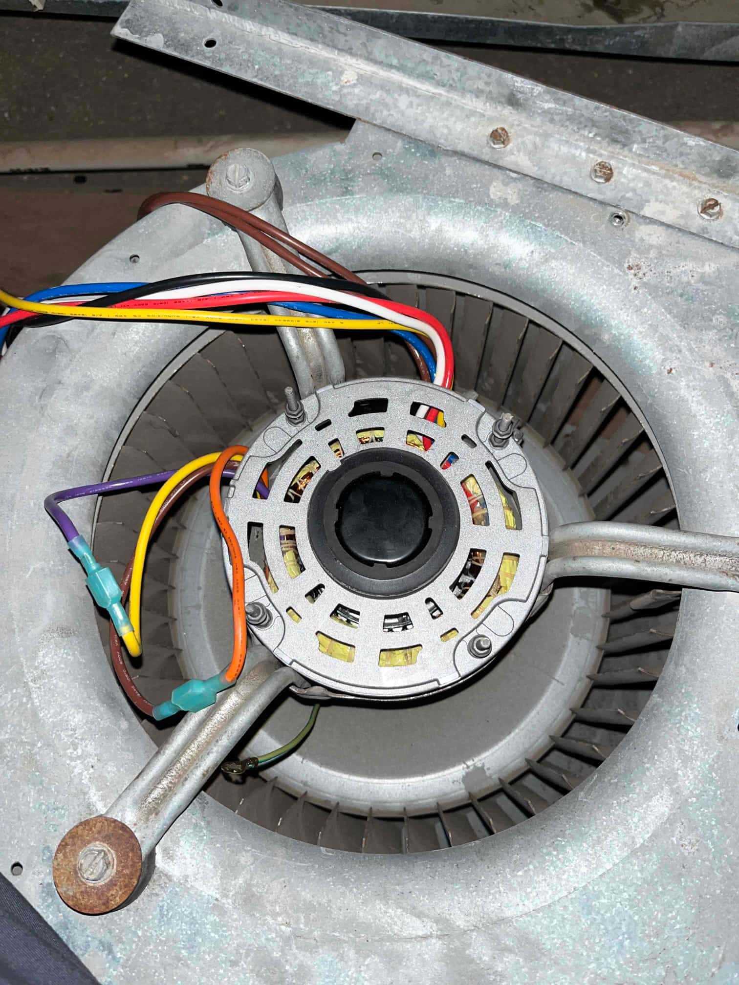 Blower assembly with exposed motor and multicolored wiring, showing rusted mounting bolts and metal housing.