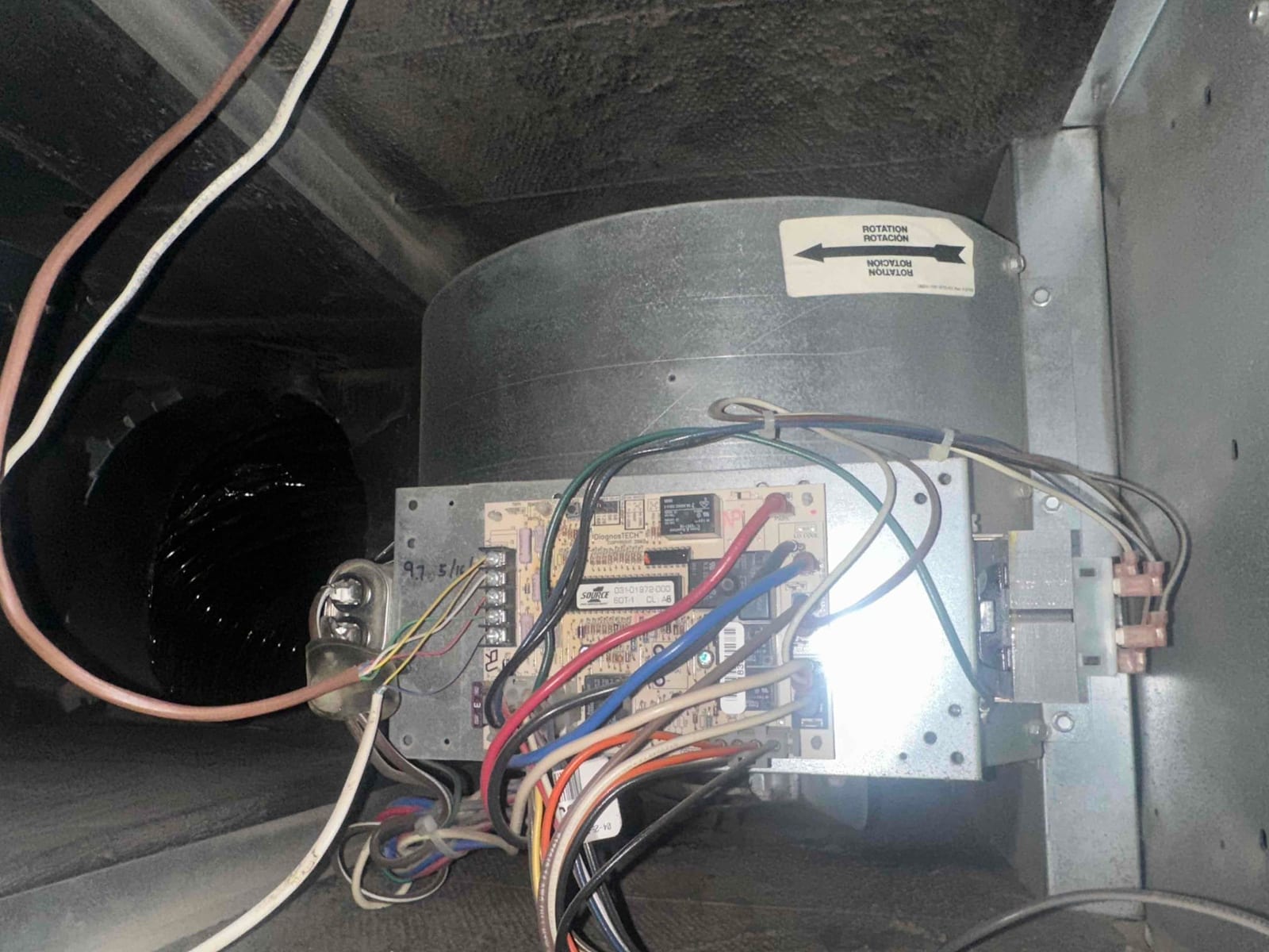 Blower housing inside air handler showing control board, connected wiring, and rotation direction label on the motor shroud.