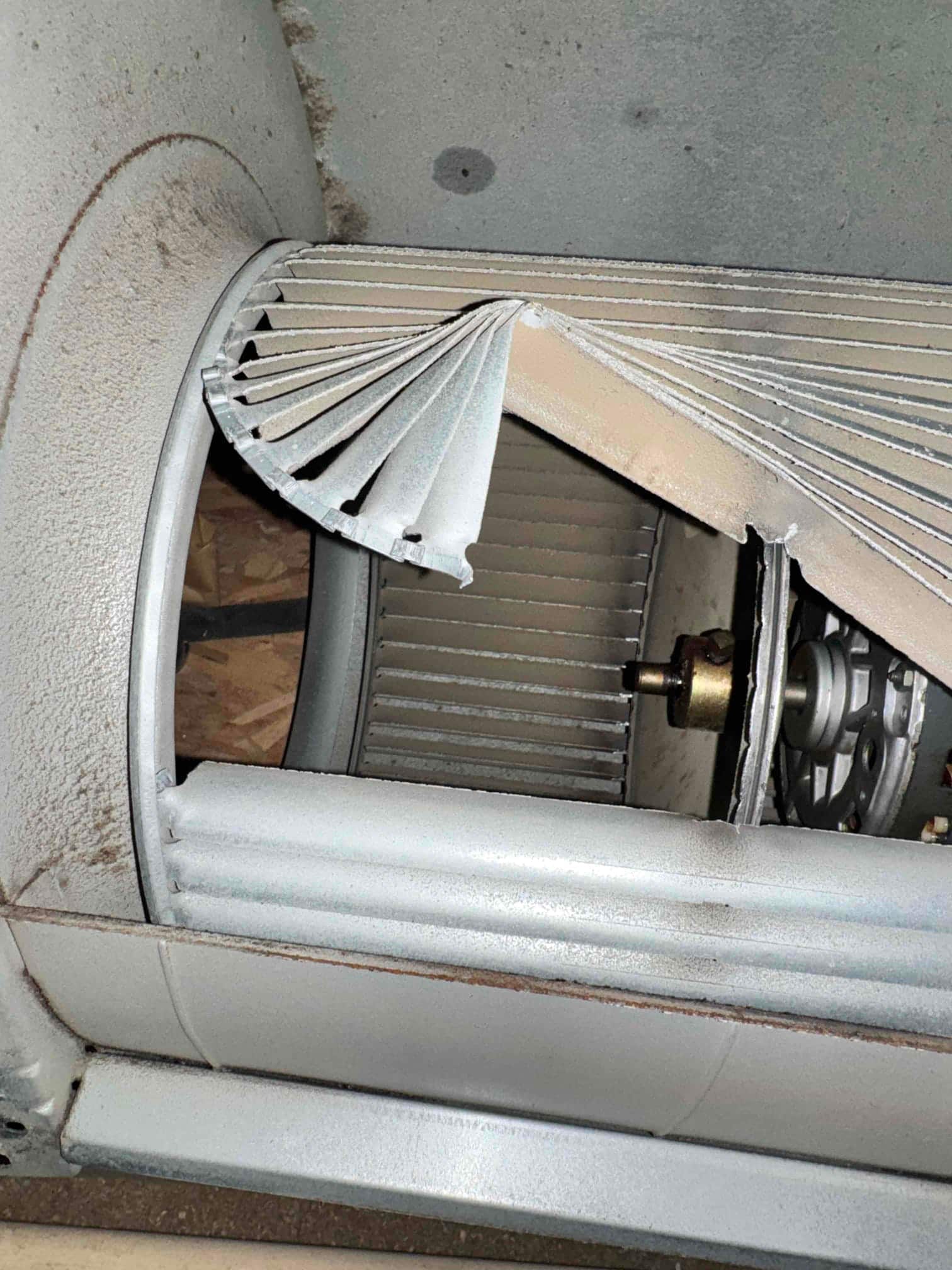 Blower wheel inside air handler showing a section of fins bent backward and deformed near motor.