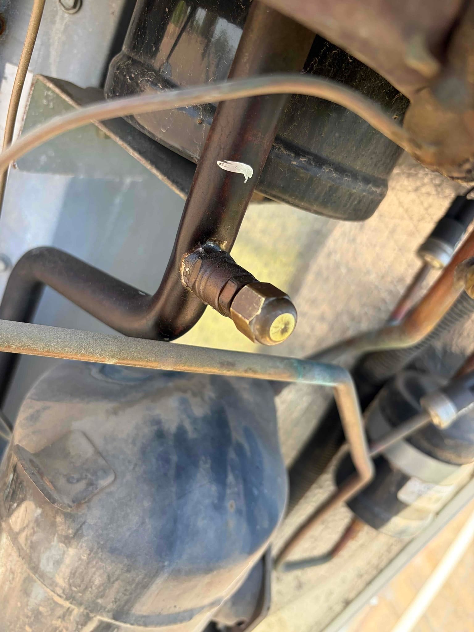 Brass service port cap on a refrigerant line near the compressor, with surrounding tubing and mounting bracket visible.