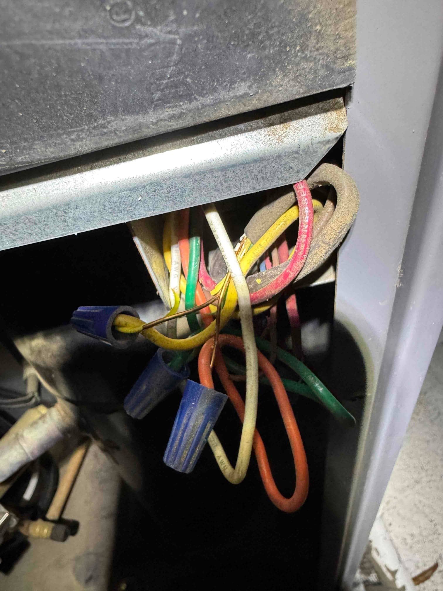 Bundle of colored wires with blue wire nuts inside the unit compartment, with one yellow conductor showing exposed copper at the connection.