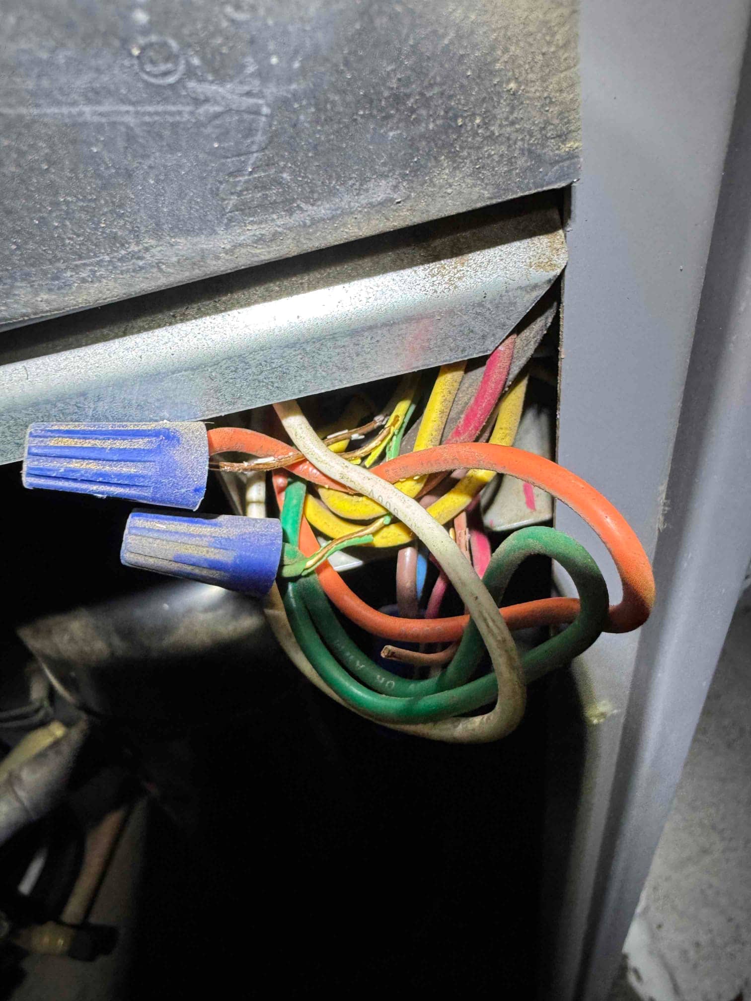 Bundle of multi-colored control wires with blue wire nuts inside metal equipment cabinet.