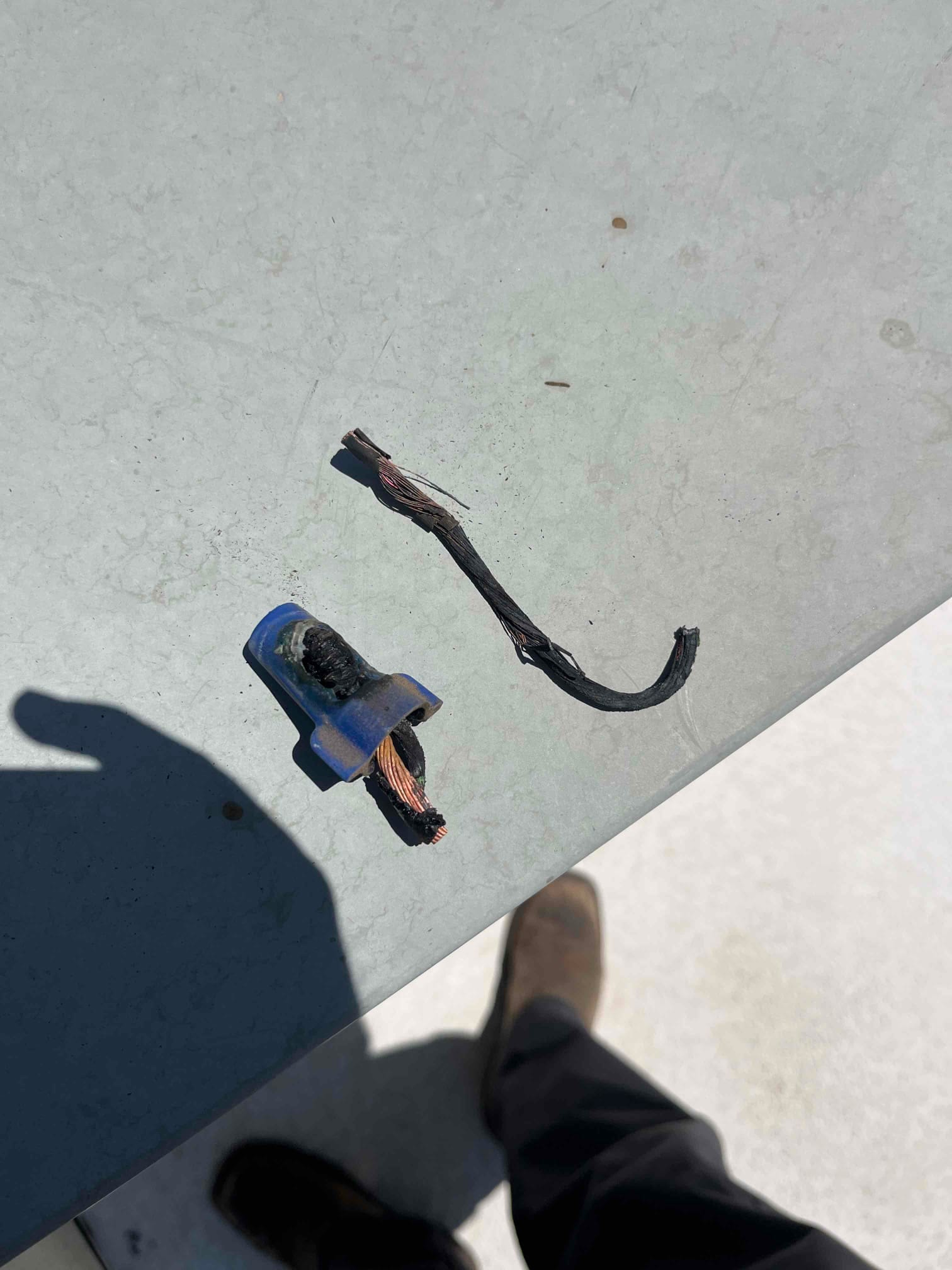 Burnt stranded copper wire segments with melted insulation and a blue crimp connector on the unit’s metal panel.