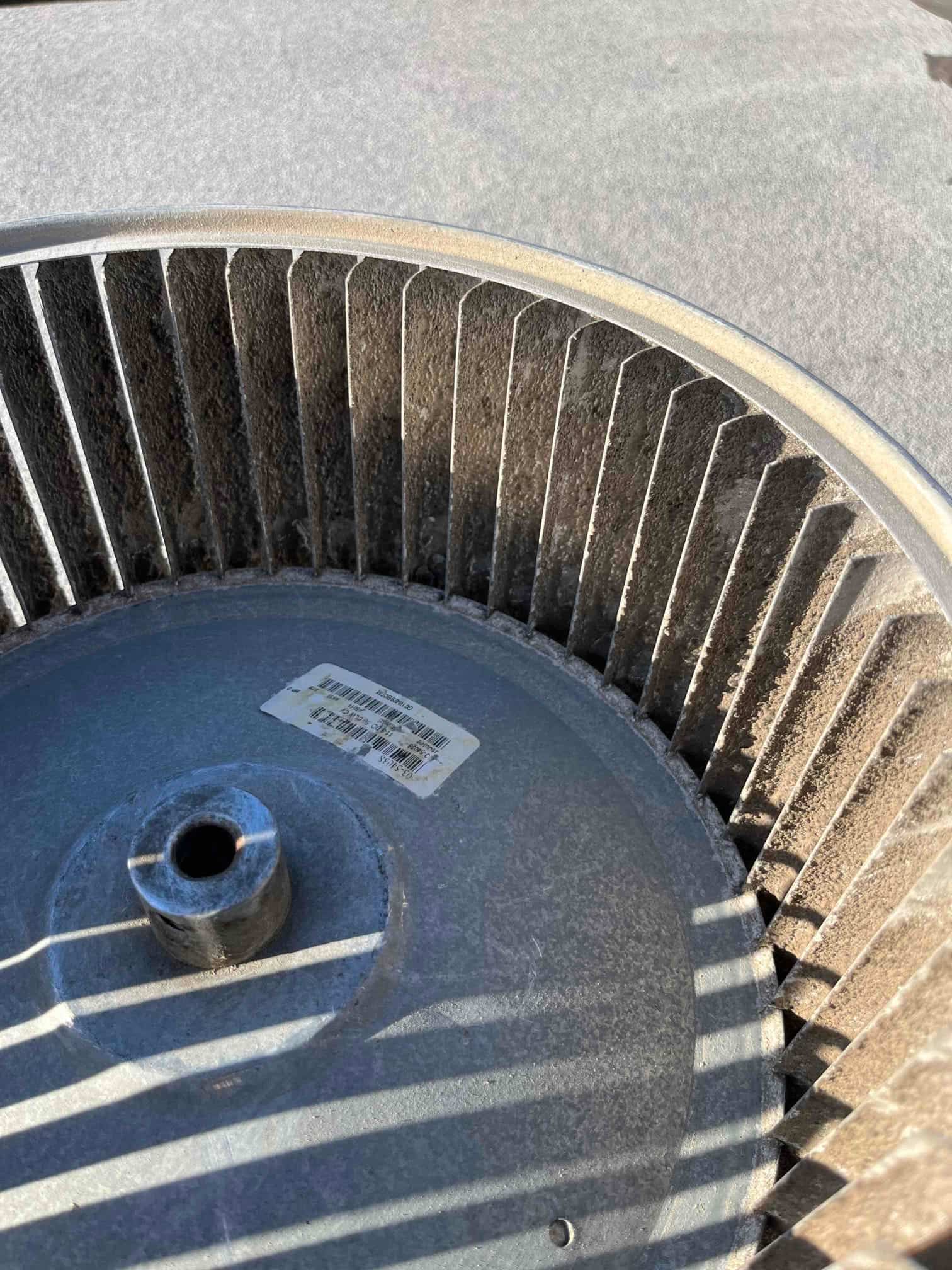 Centrifugal blower wheel with accumulated dust on blades and a barcode label on the hub.
