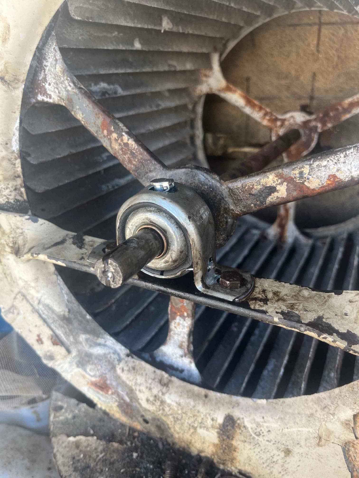 Centrifugal blower wheel and shaft with pillow block bearing mounted on a rusted support bracket.
